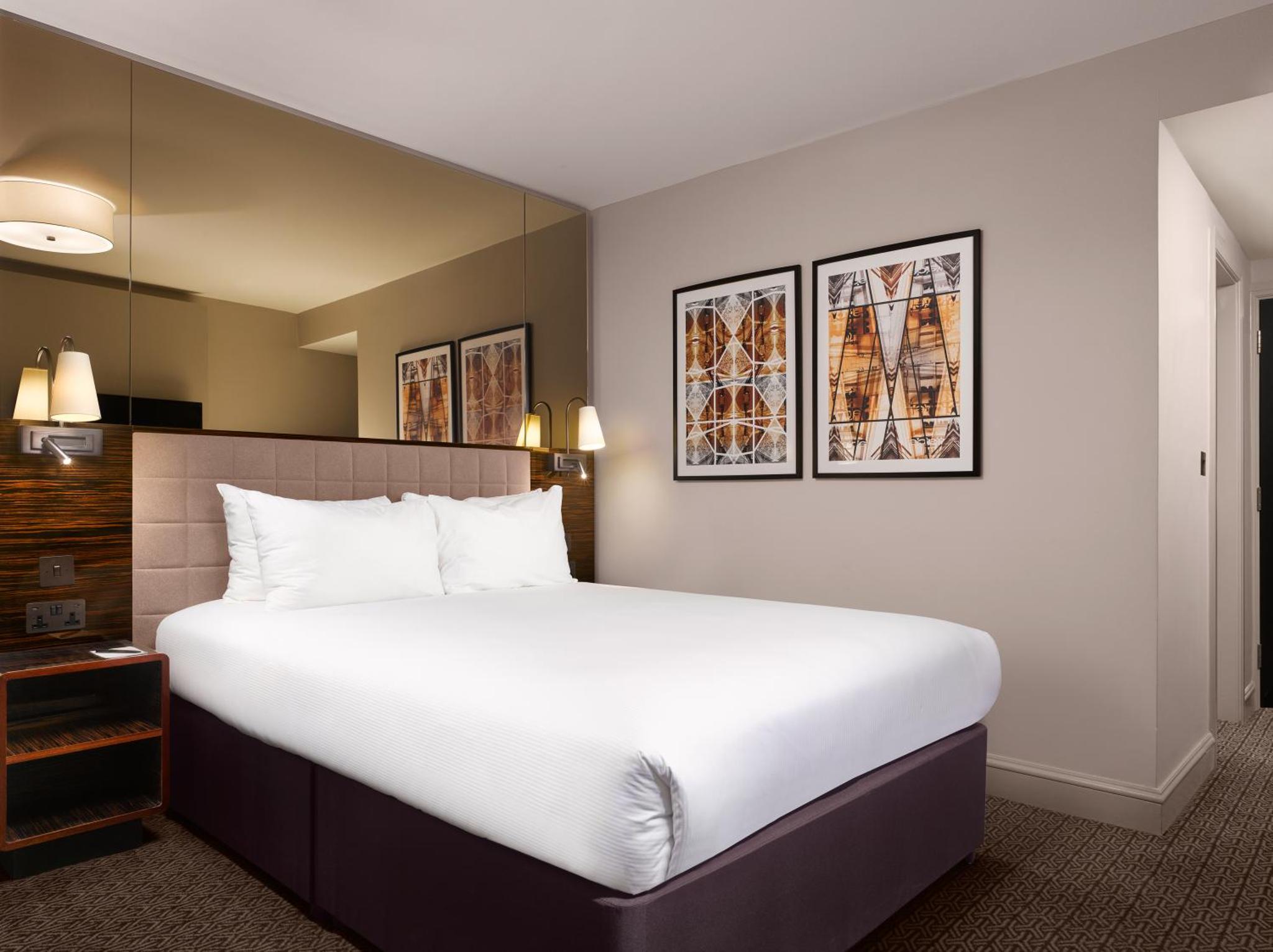 a hotel room with a large bed and pictures on the wall at Strand Palace in London