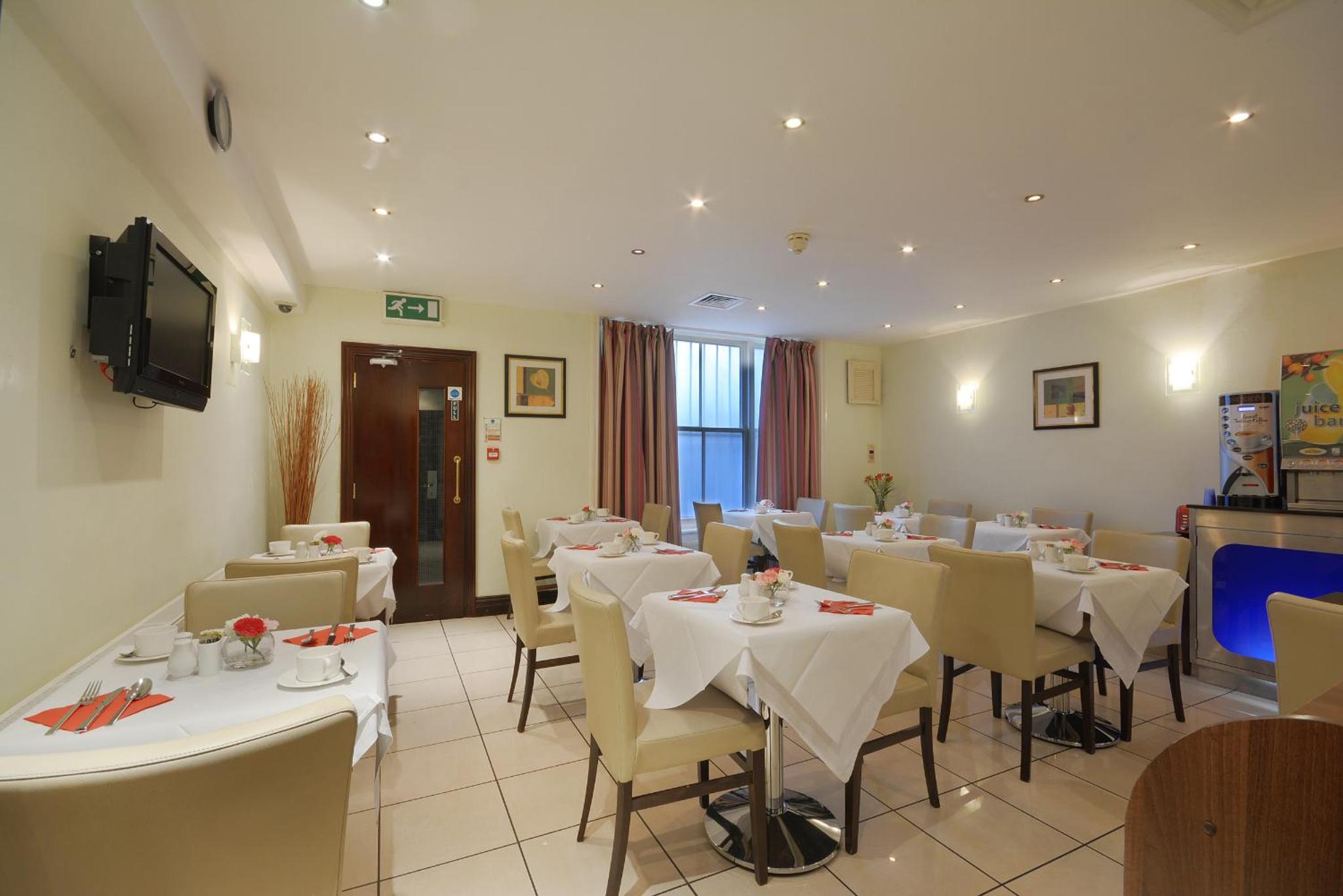 a restaurant with white tables and chairs and a television at The Premier Notting Hill in London