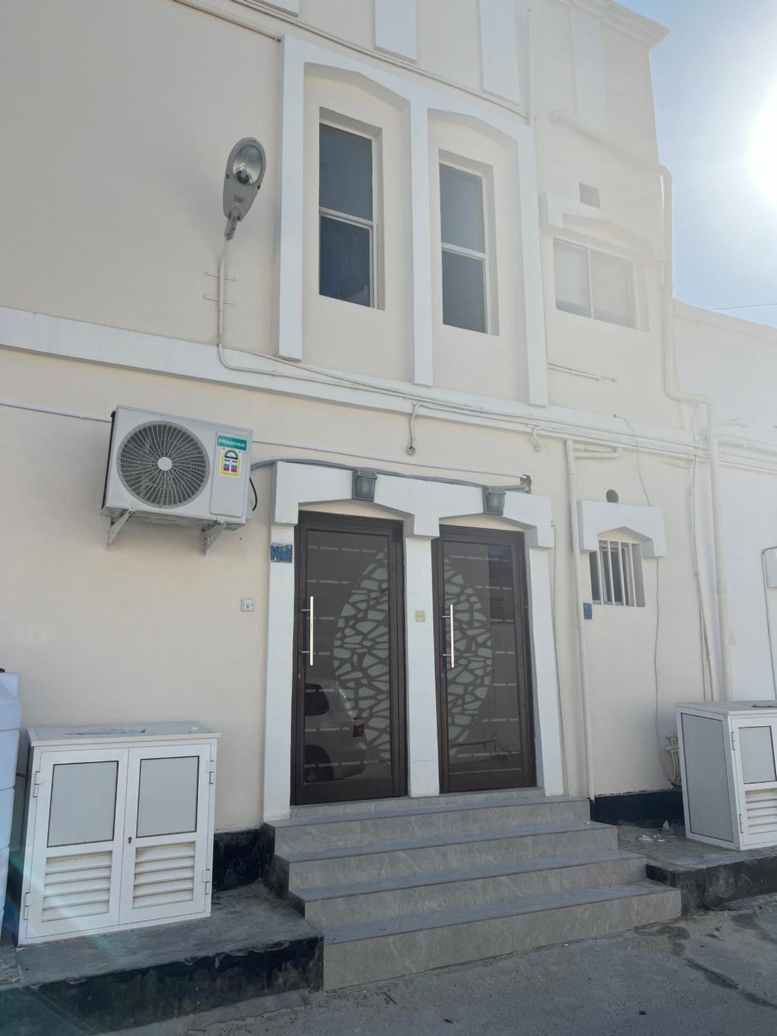 a white building with a door and a fan at AlWadi AGROSERNE - 2BR West Riffa Apartment in Ar Rifā‘
