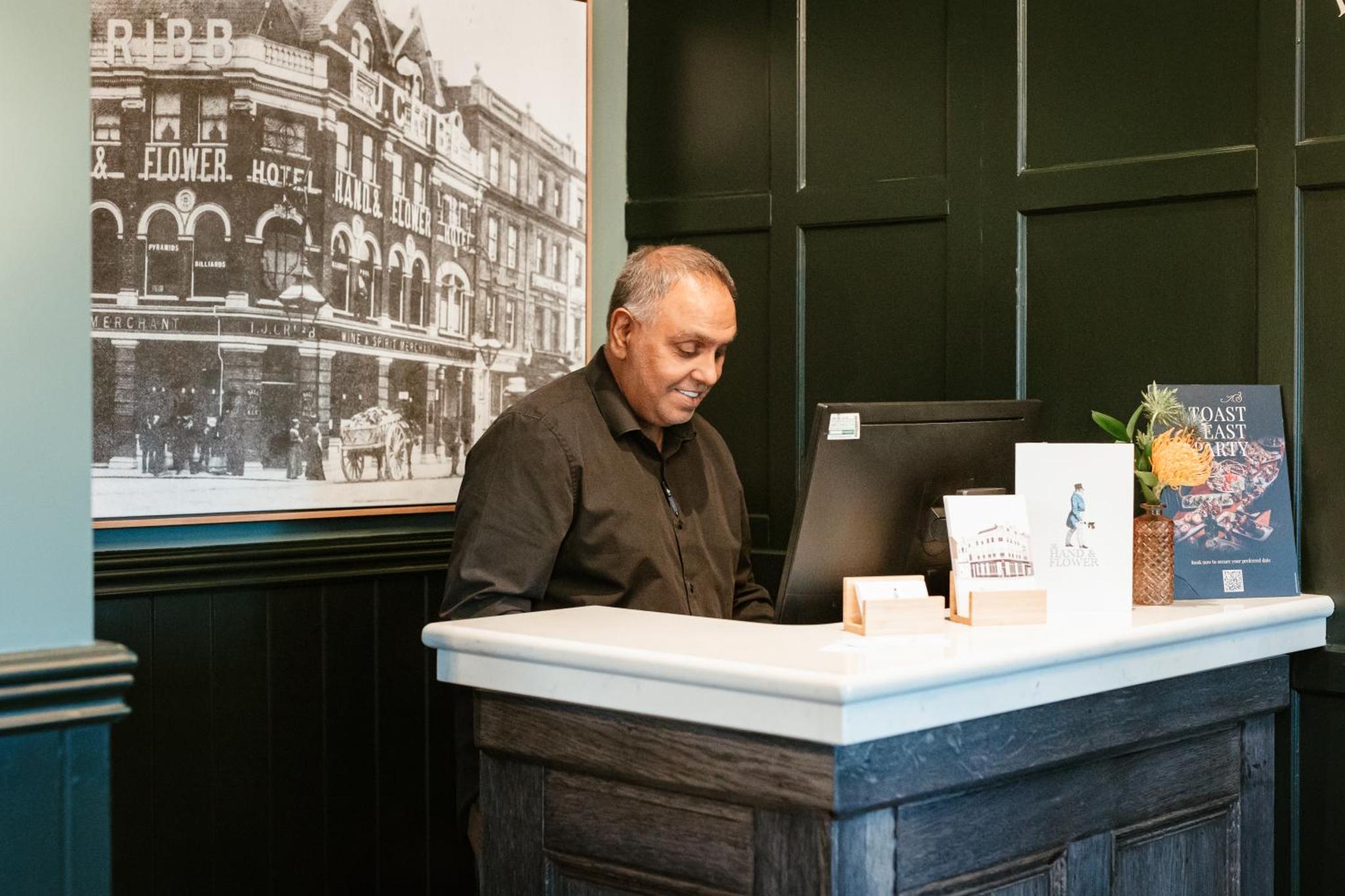 a man standing at a table with a laptop computer at Hand & Flower in London