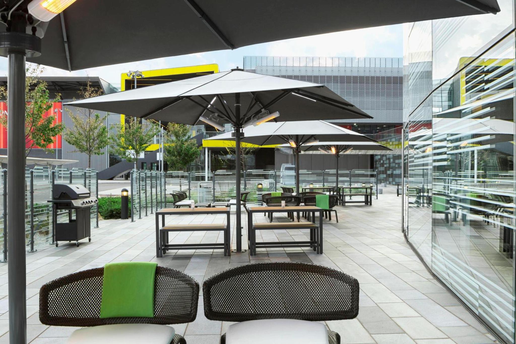a patio with tables and chairs with umbrellas at Aloft London Excel in London