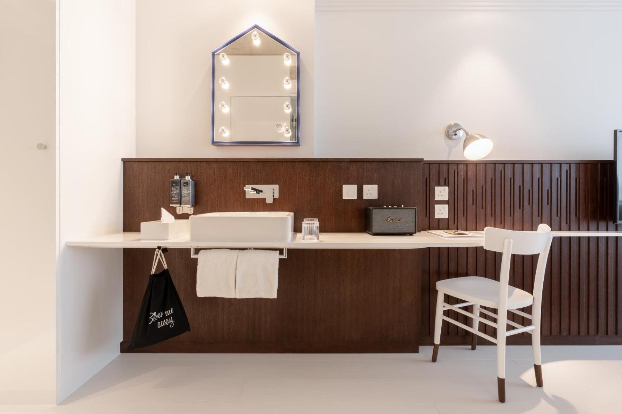 a bathroom with a counter with a sink and a chair at Ruby Zoe Hotel London in London +63 photos