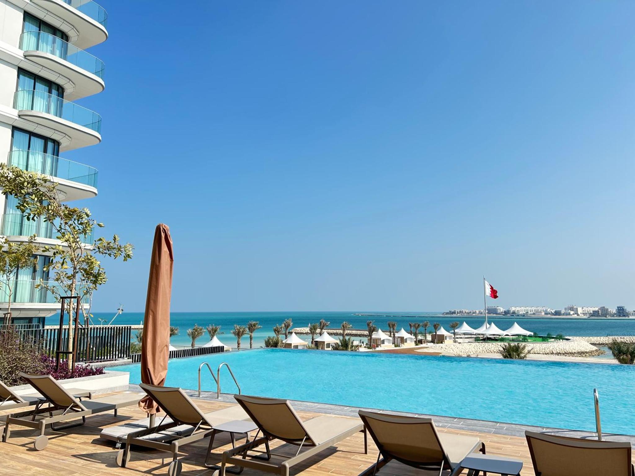a swimming pool with lounge chairs and the ocean at Address Residence Marassi Vista Bahrain in Muharraq
