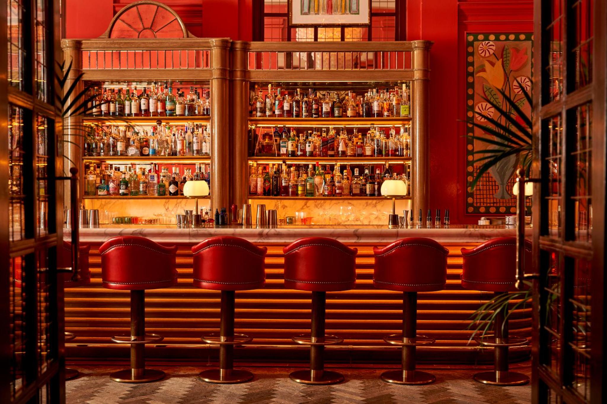 a bar with red chairs in front of a bar at The Bloomsbury Hotel in London
