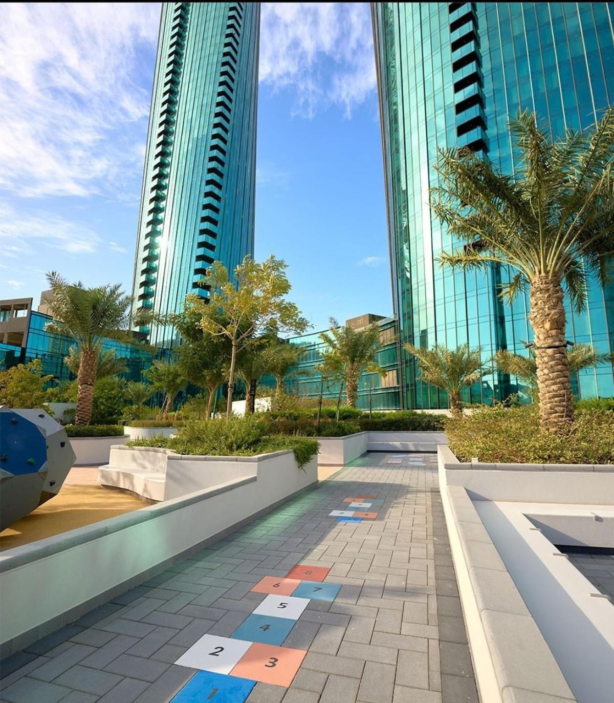 a walkway with palm trees in front of tall buildings at TOP Luxurious and Cozy 2BR with 5 mins to Bahrain Bay in Manama