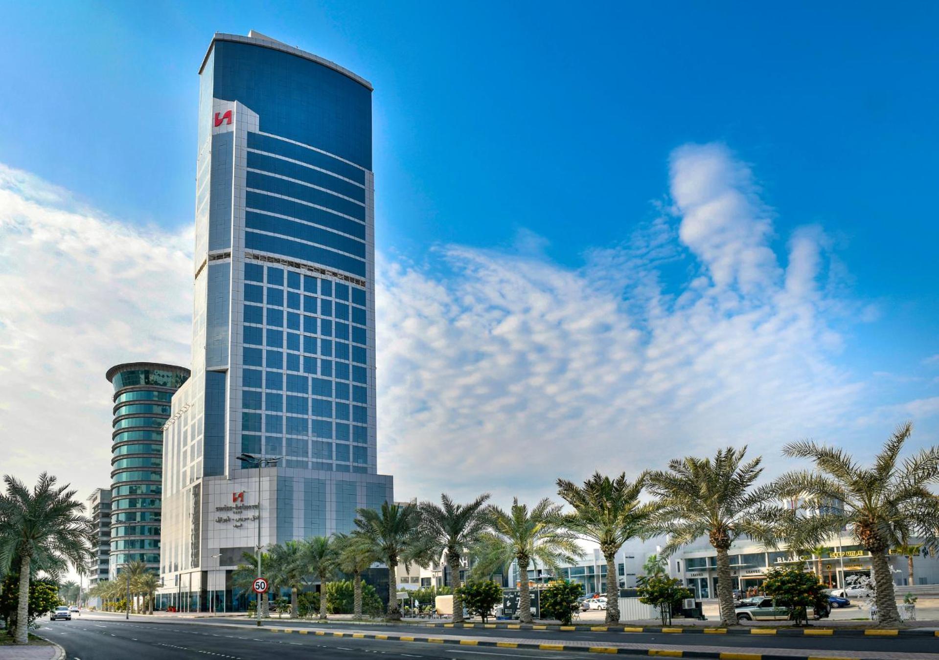 a tall blue building with palm trees in front of it at Swiss-Belhotel Seef Bahrain in Manama