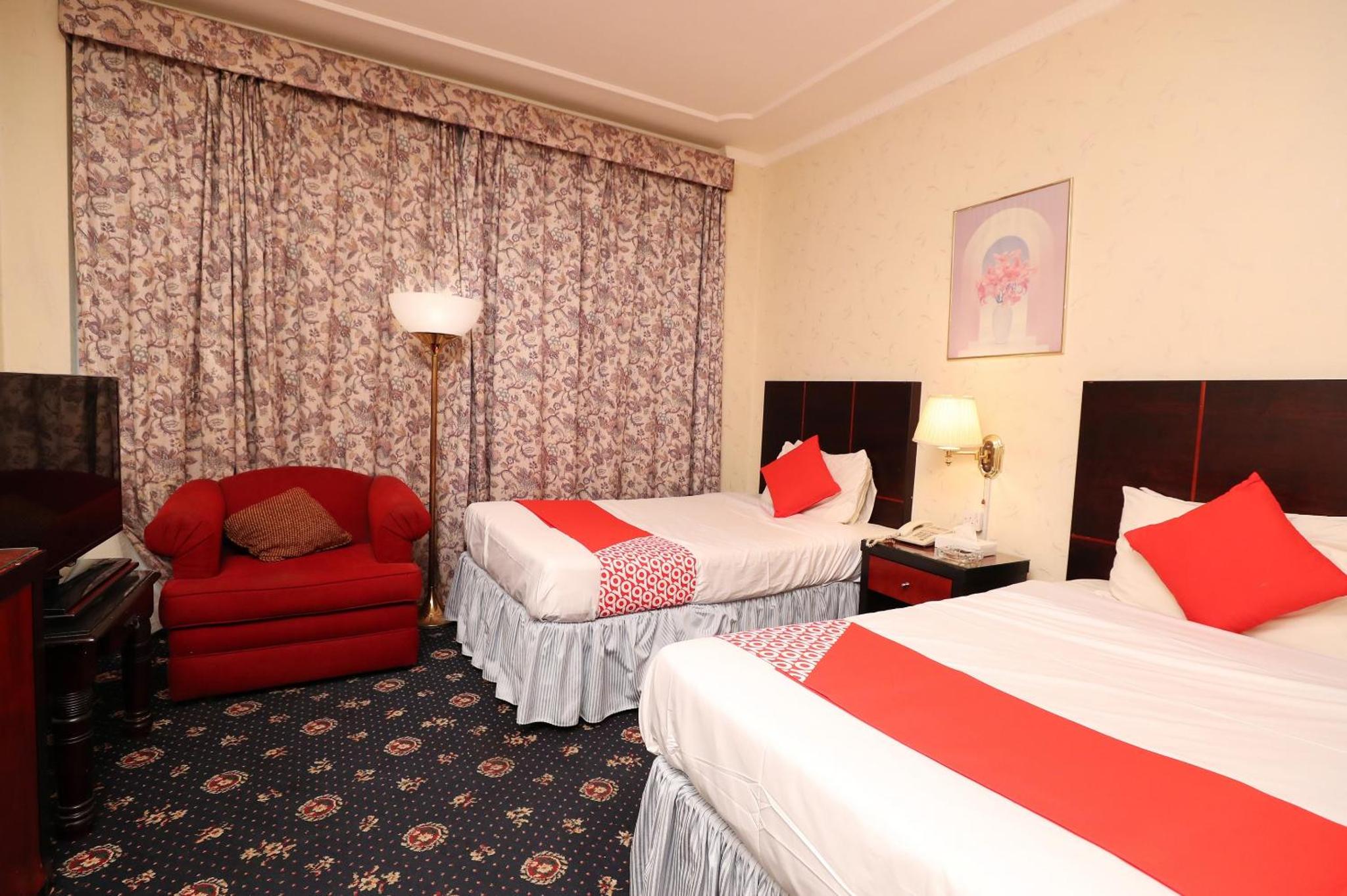 a hotel room with two beds and a red chair at OYO 112 Semiramis Hotel in Manama