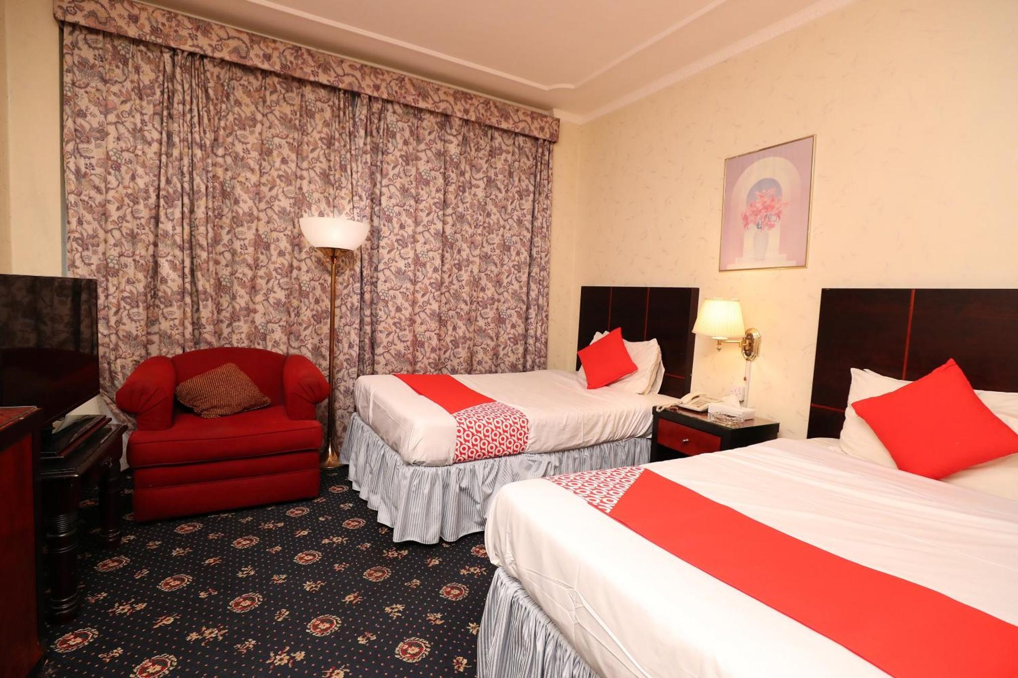 a hotel room with two beds and a red chair at OYO 112 Semiramis Hotel in Manama