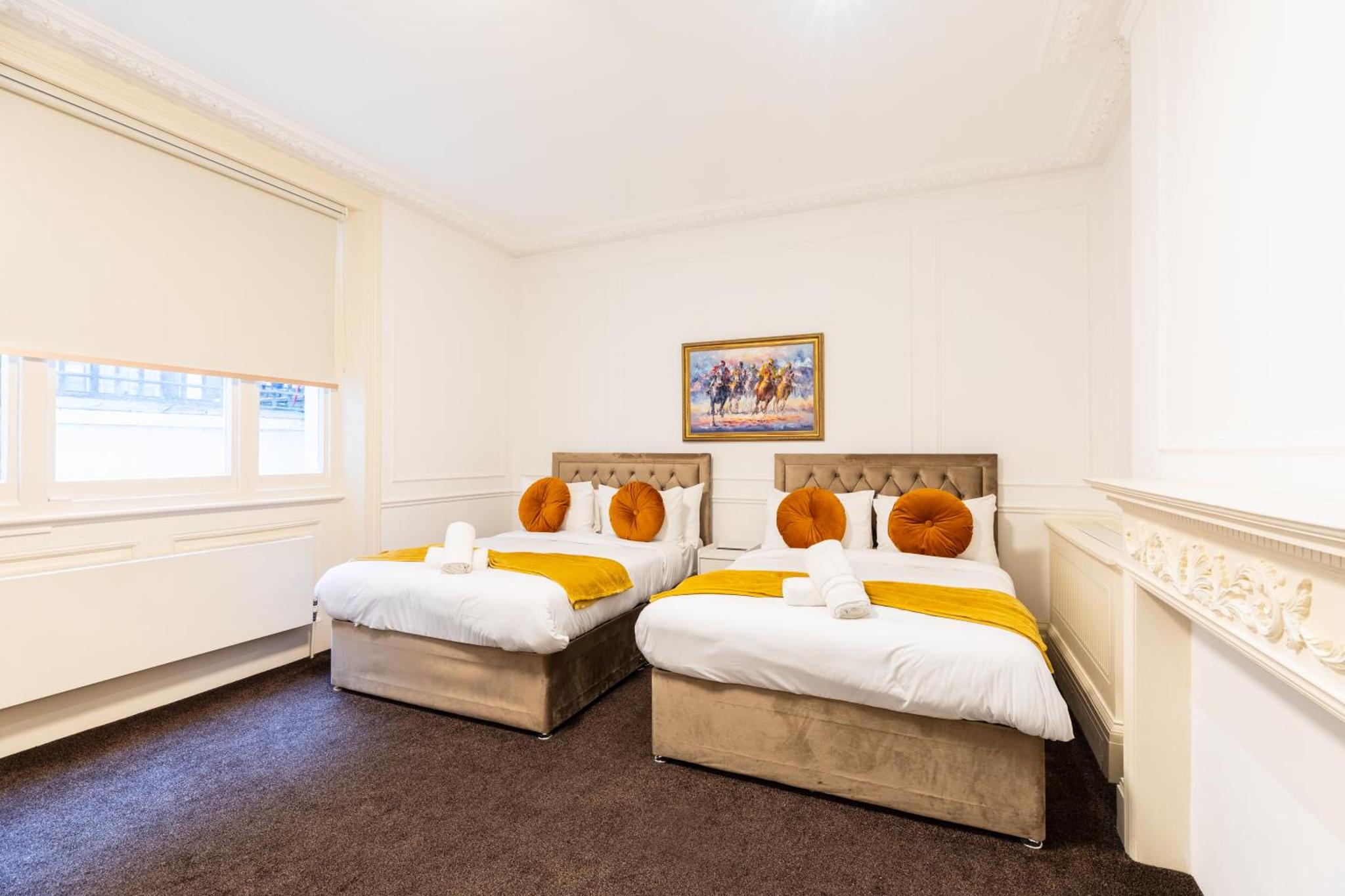 two beds in a room with white walls and a window at Mayfair Residences in London