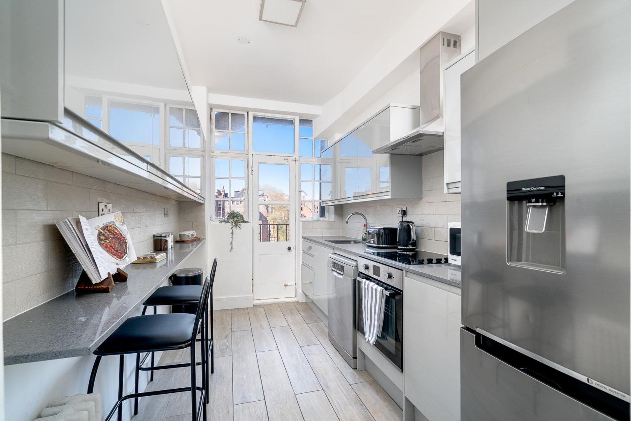 a kitchen with white appliances and a counter with stools at Elegant 4 Bed Flat Opposite Hyde Park in London