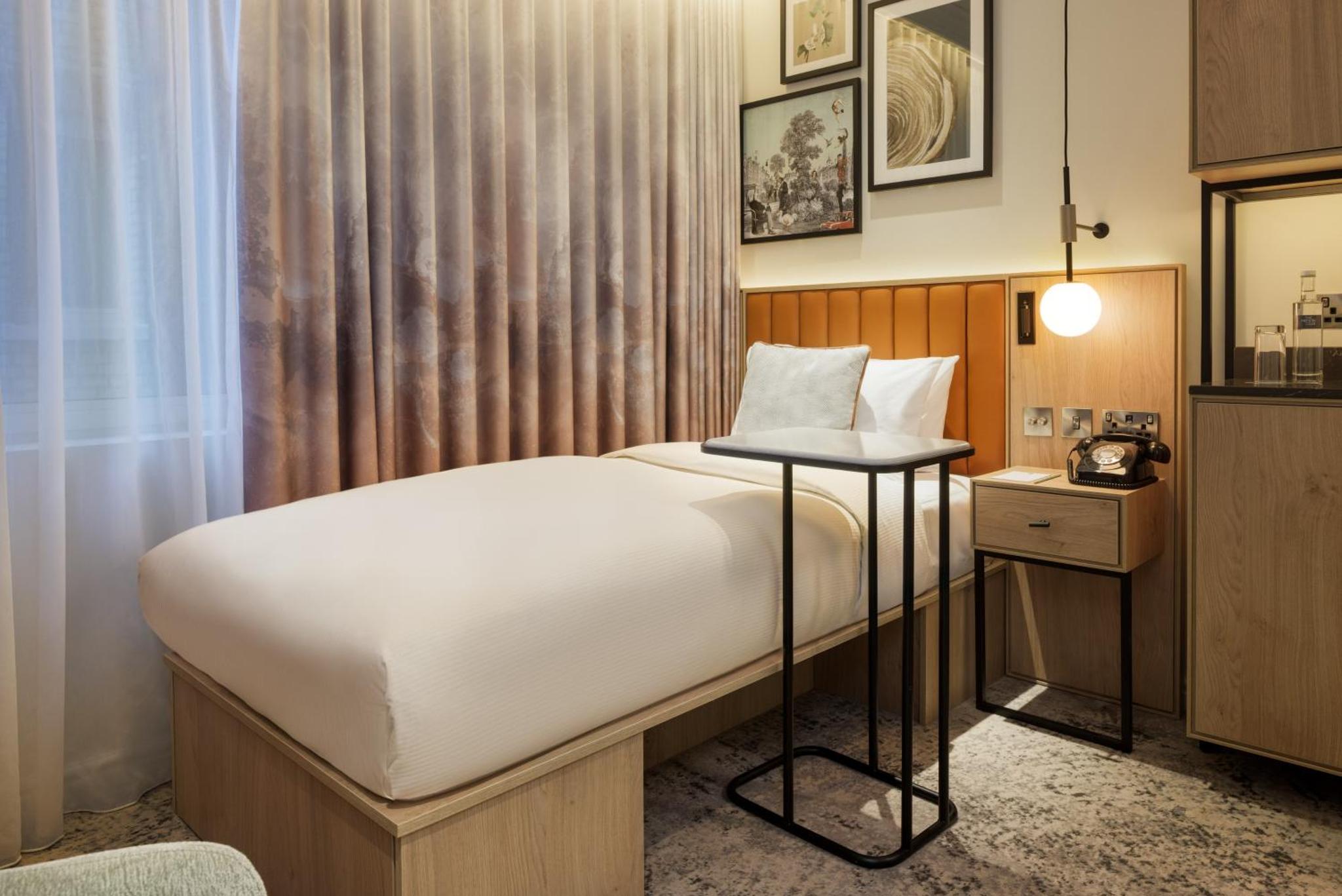 a bedroom with a bed with a table in it at The Memoir Club, formerly Ambassadors Bloomsbury in London