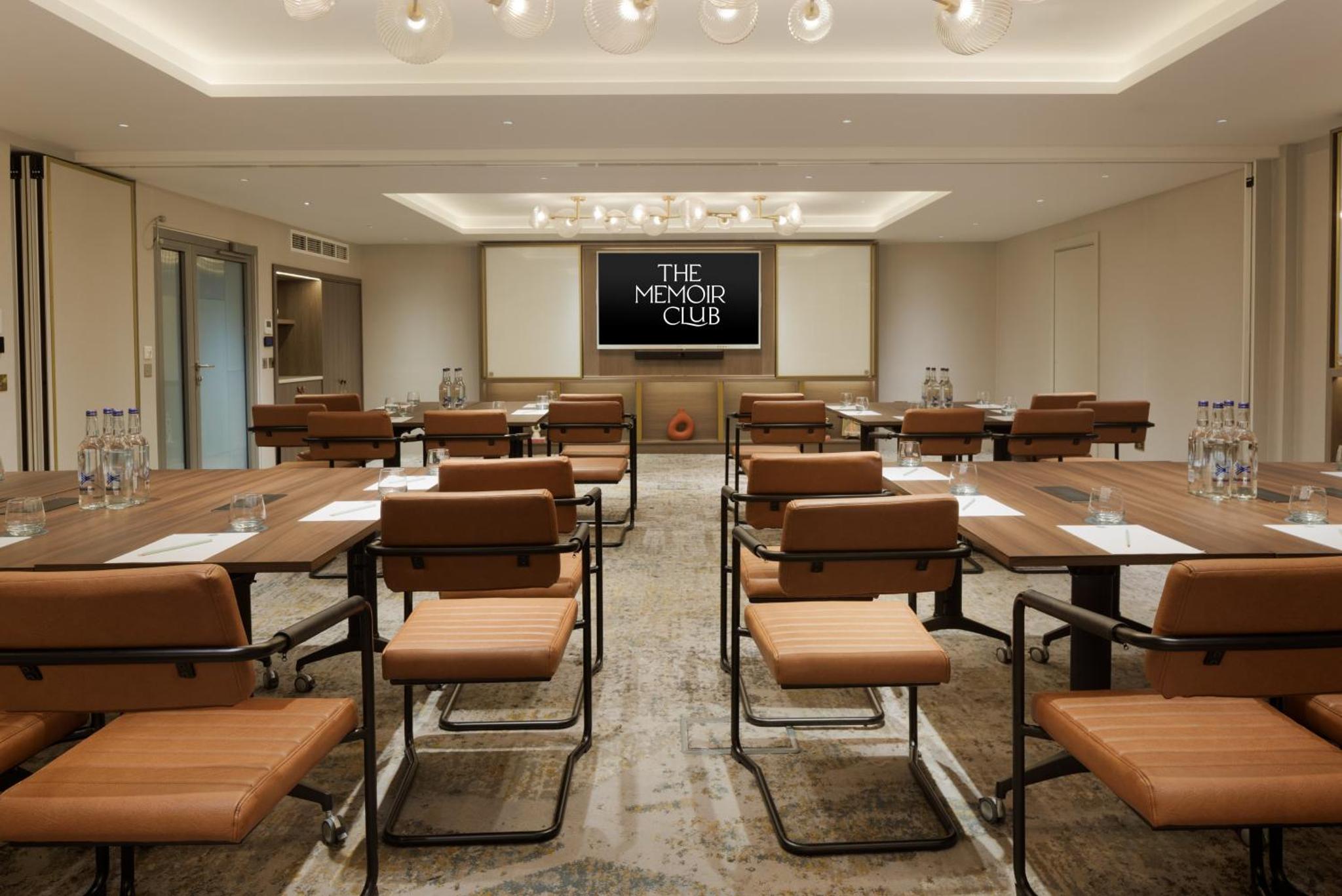 a conference room with tables and chairs and a projection screen at The Memoir Club, formerly Ambassadors Bloomsbury in London