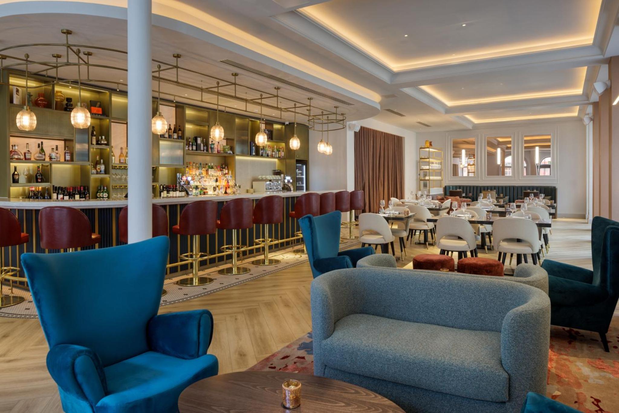 a restaurant with blue chairs and a bar at The Memoir Club, formerly Ambassadors Bloomsbury in London