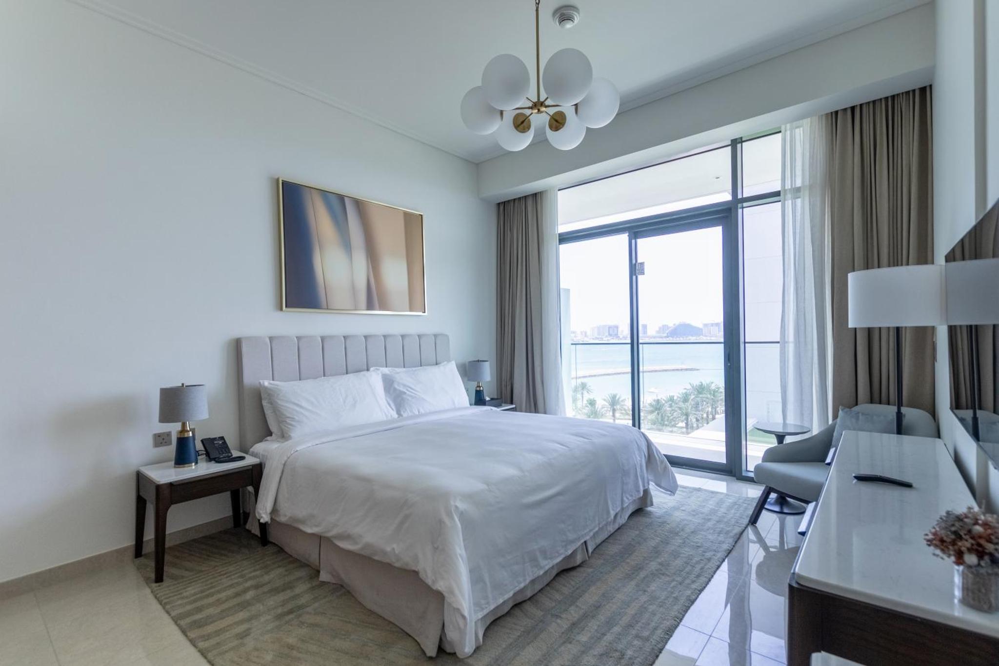 a white bedroom with a bed and a large window at Premium Apartments at Address Resort Residendtial Building in Muharraq