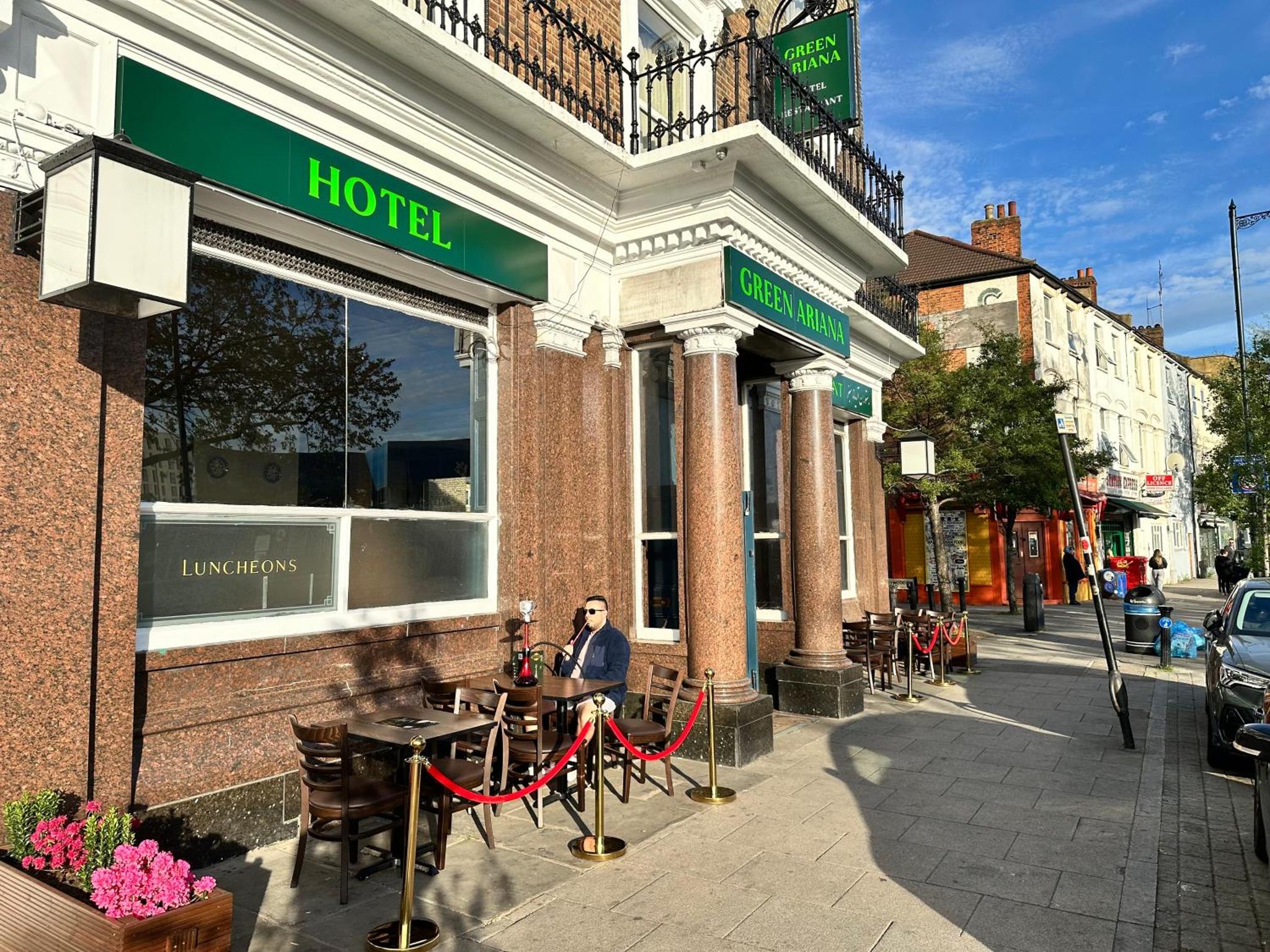a man sitting at a table outside of a hotel at Green Ariana Hotel - near Wembley and central London in London