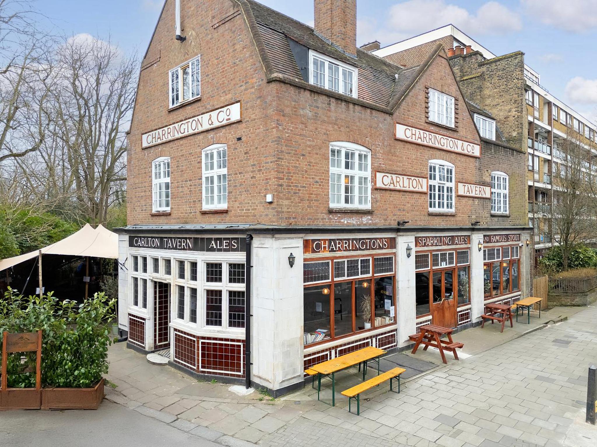 a large brick building with benches in front of it at The Carlton Tavern Hotel in London