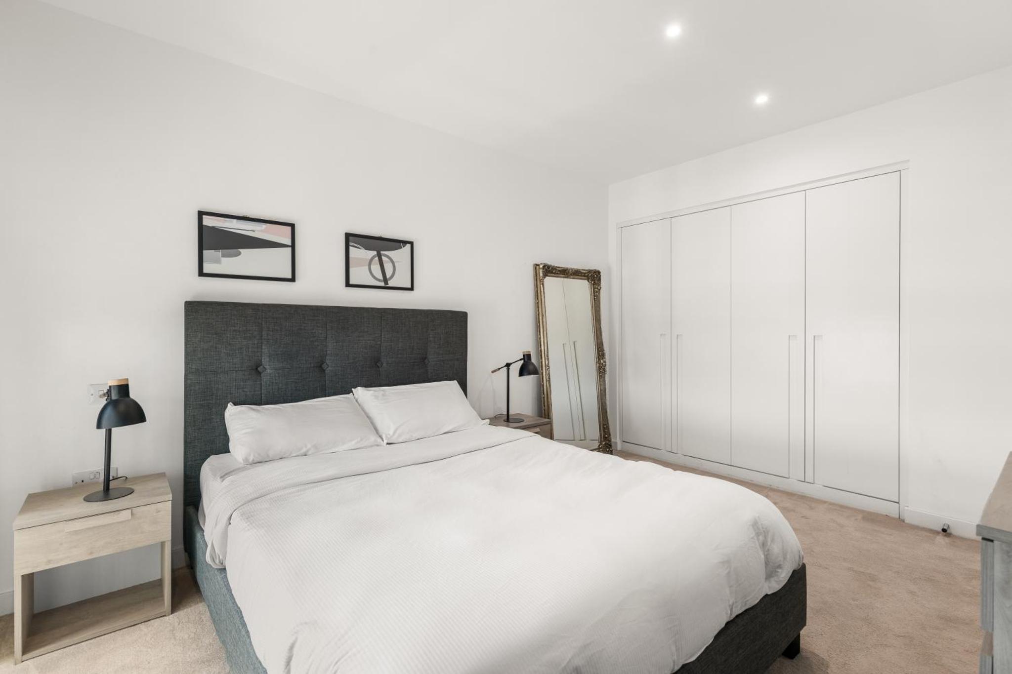 a white bedroom with a large bed and a mirror at Spacious modern 1 bed Apartment. in London
