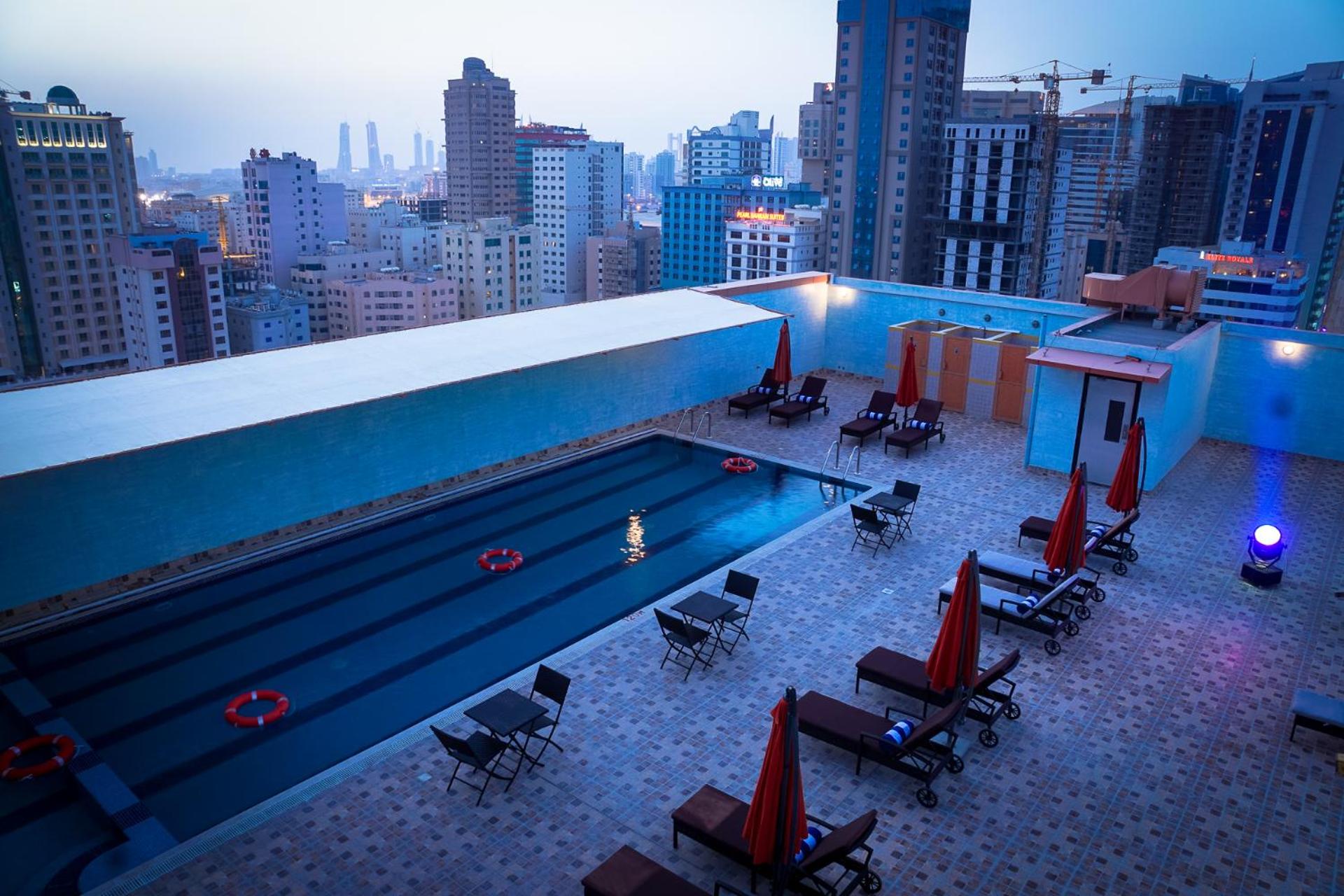 a swimming pool on top of a building with chairs at Arman Hotel Juffair Mall in Manama