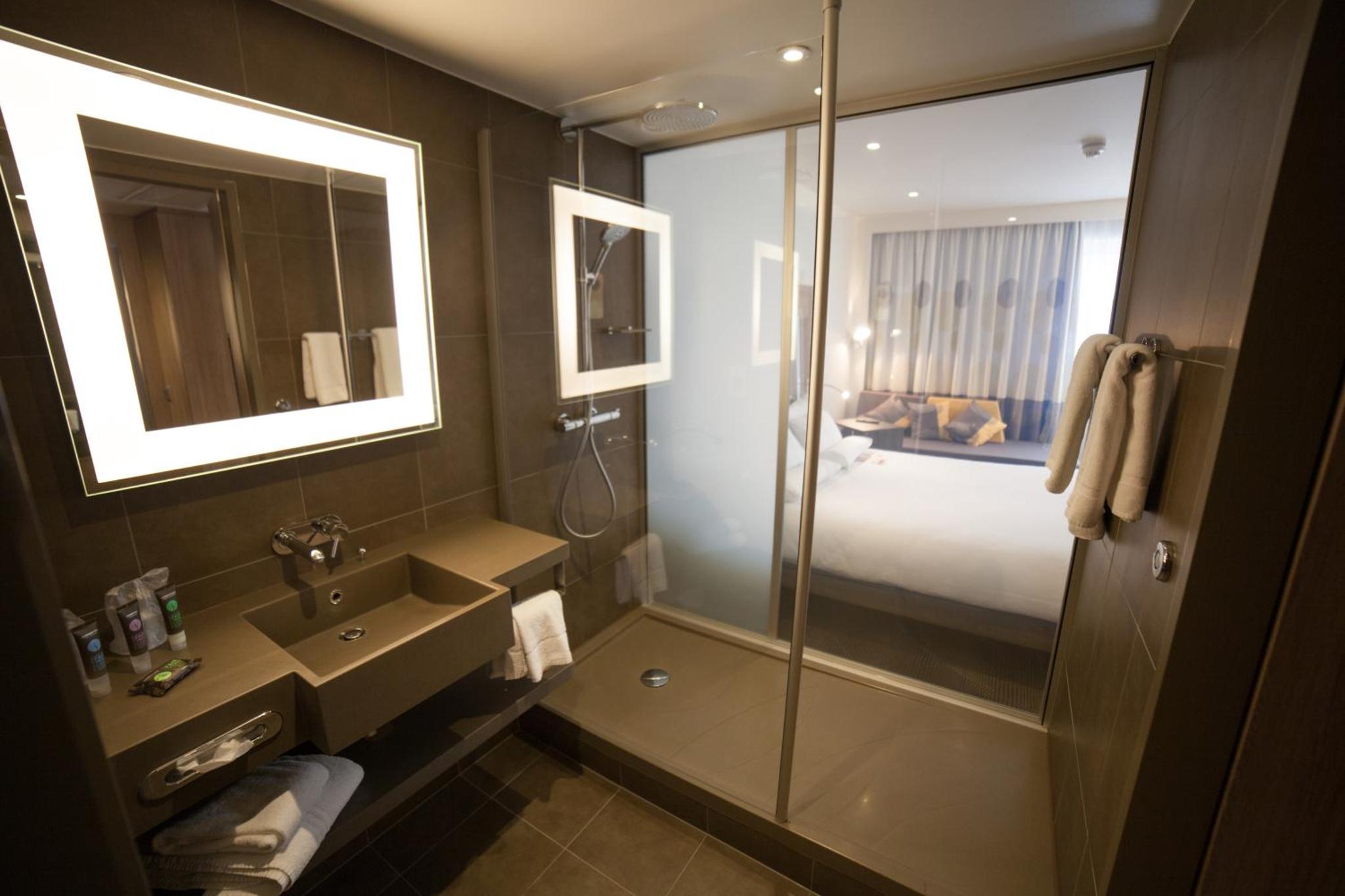 a bathroom with a shower and a sink and a bed at Novotel London Waterloo in London