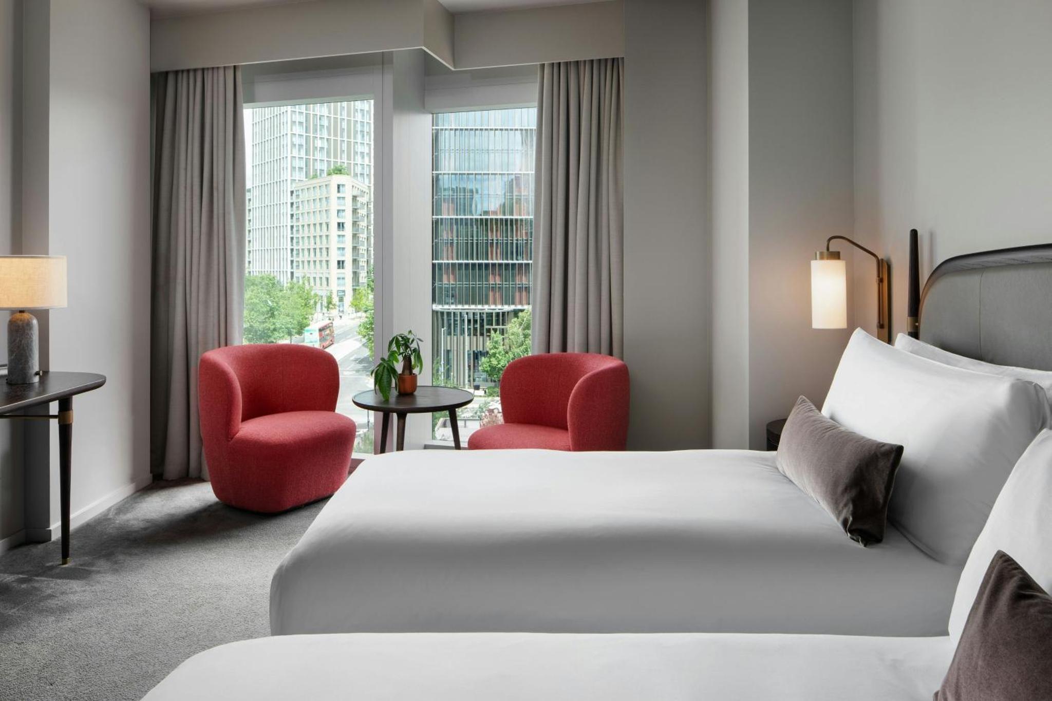 a hotel room with a bed and two red chairs at The Stratford, Autograph Collection in London