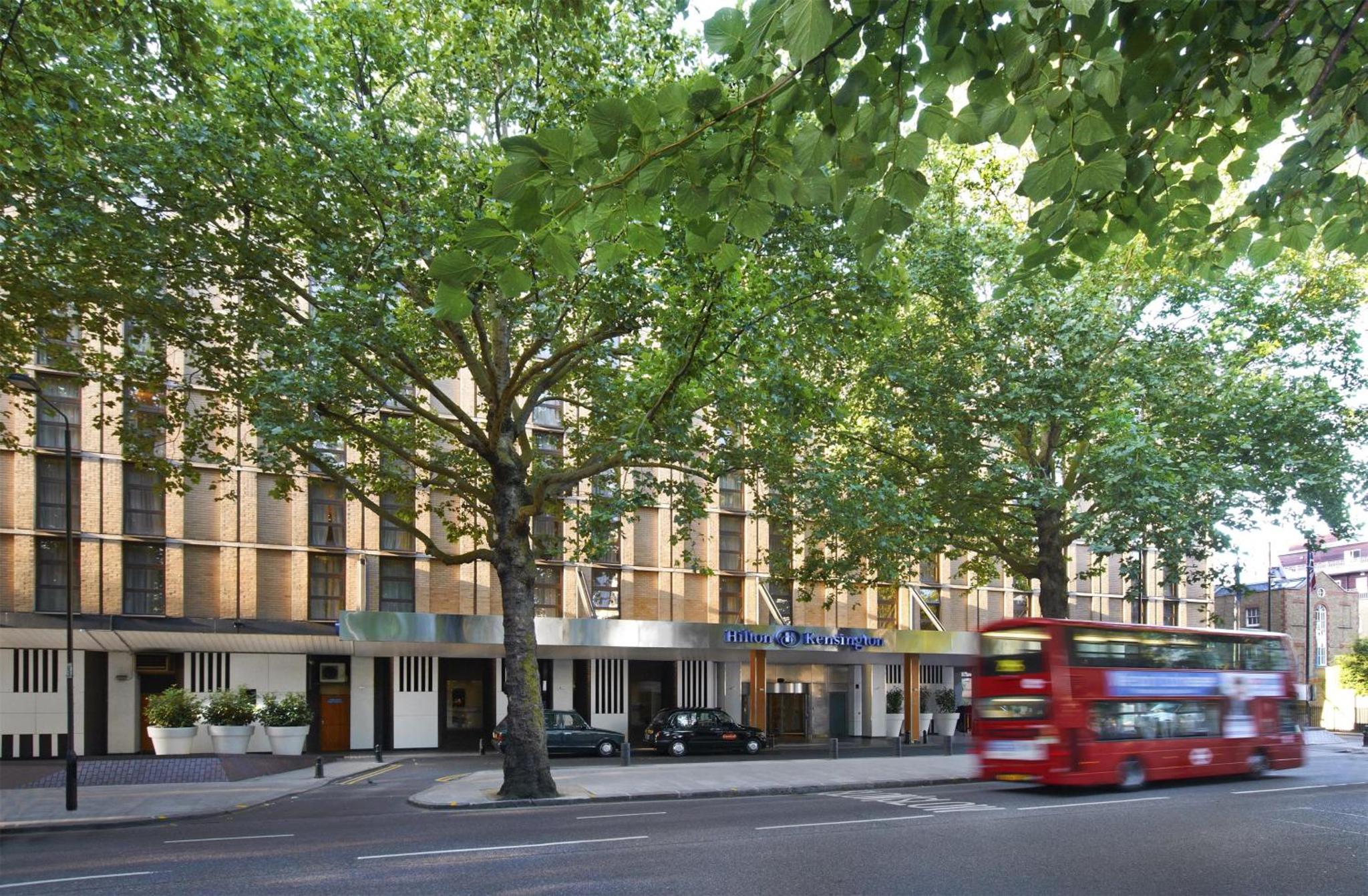 a red double decker bus parked in front of a building at Hilton London Kensington Hotel in London
