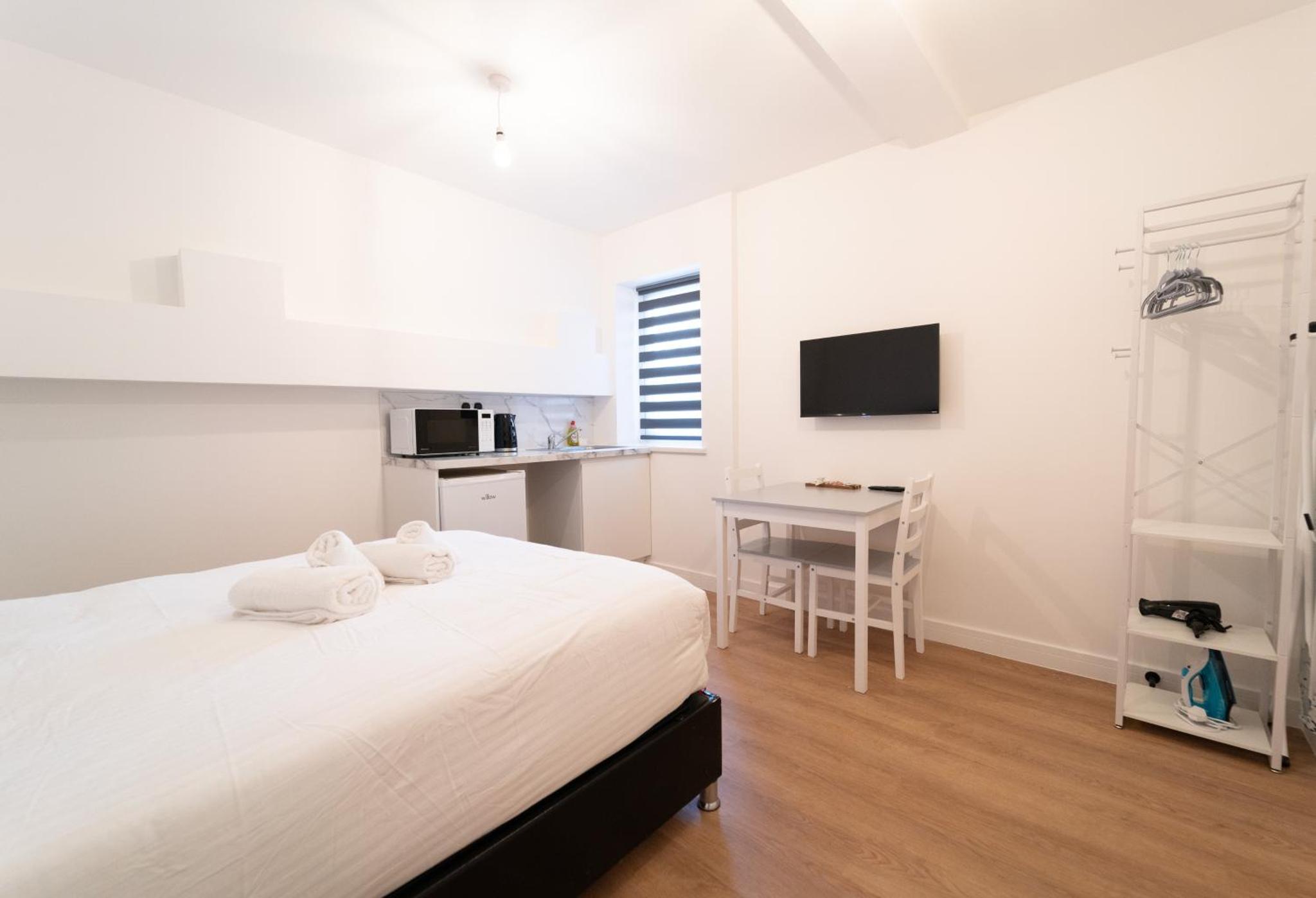 a white bedroom with a bed and a desk at Centra High Road in London