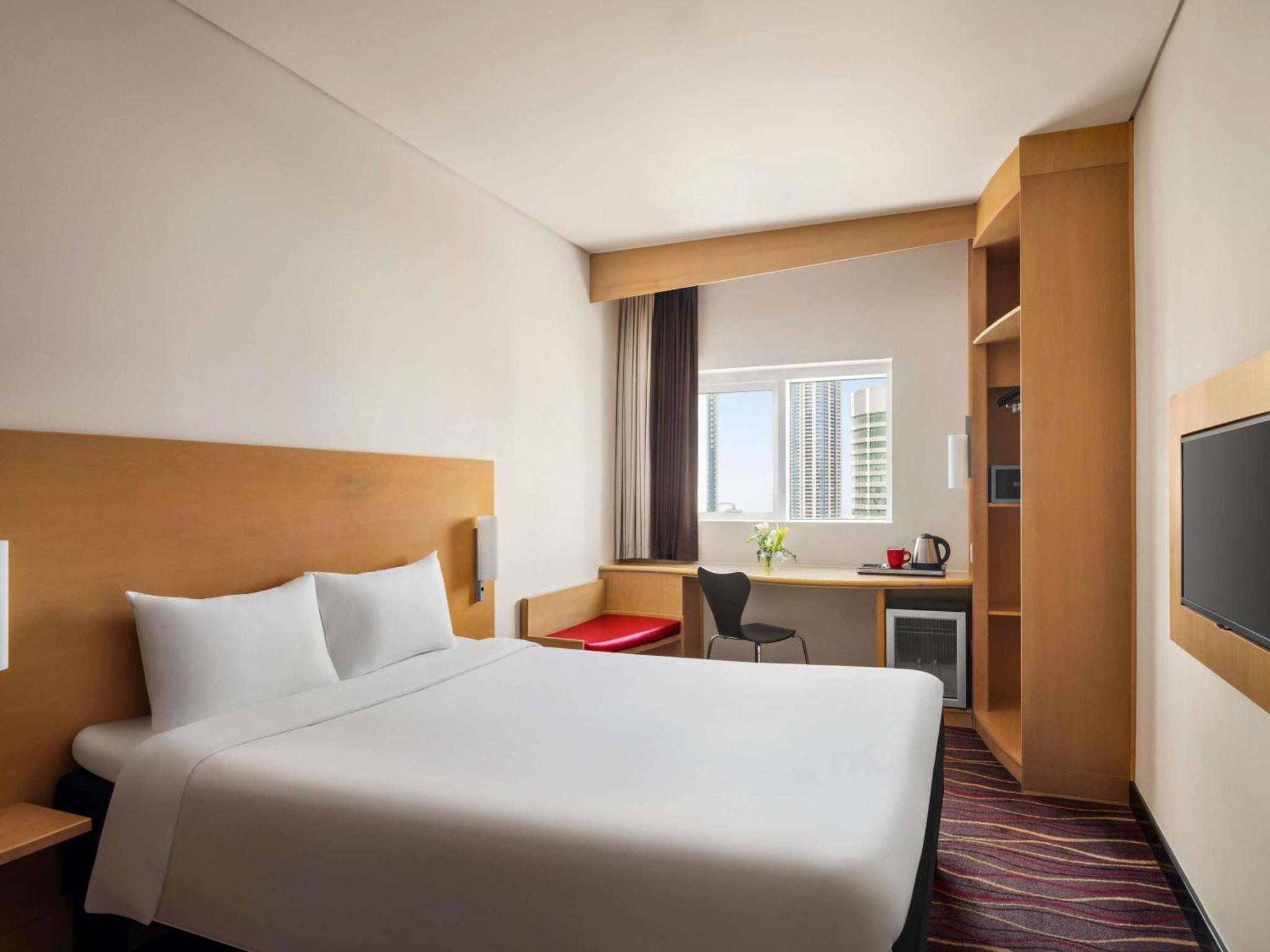 a hotel room with a white bed and a desk at ibis Seef Manama in Manama