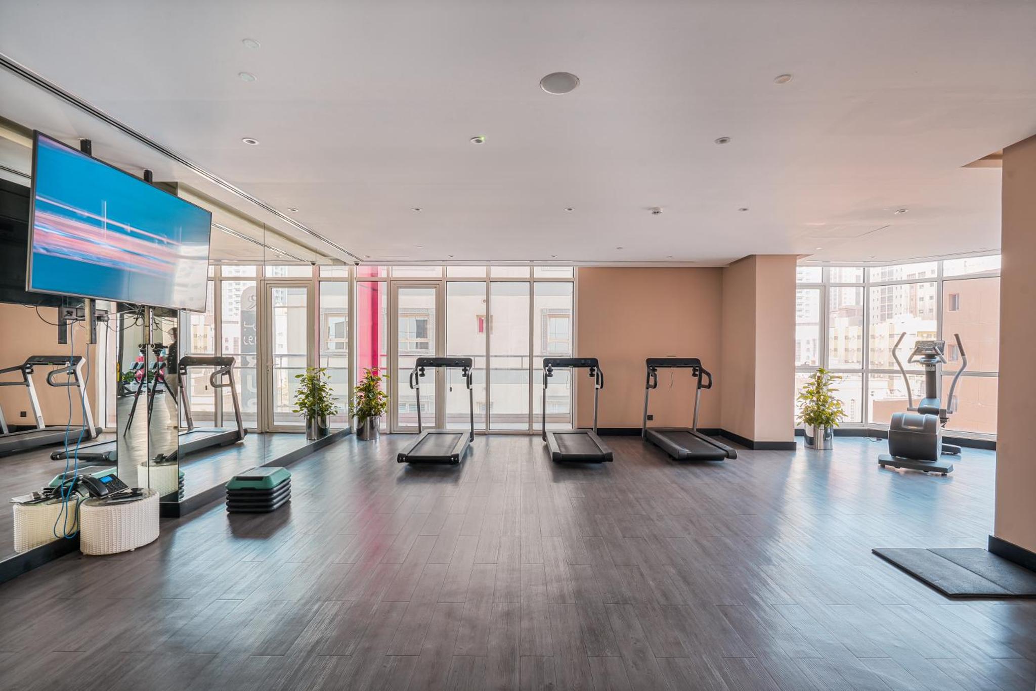 a gym with treadmills and a flat screen tv at Eden Garden Hotel Apartment in Manama