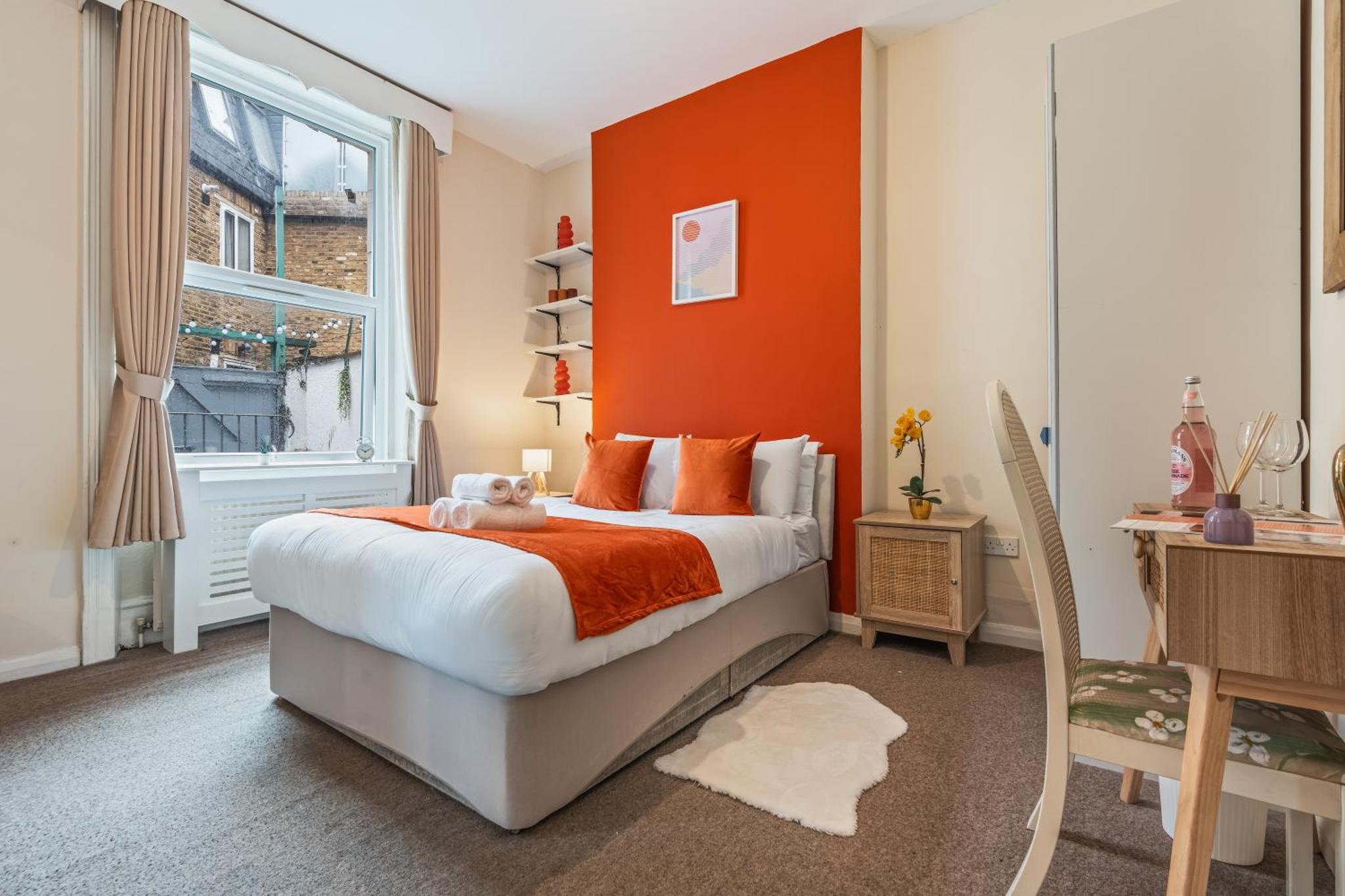 a bedroom with a bed with an orange wall at Stylish 3 Bed Fulham Sleeps 10, Stamford Bridge in London