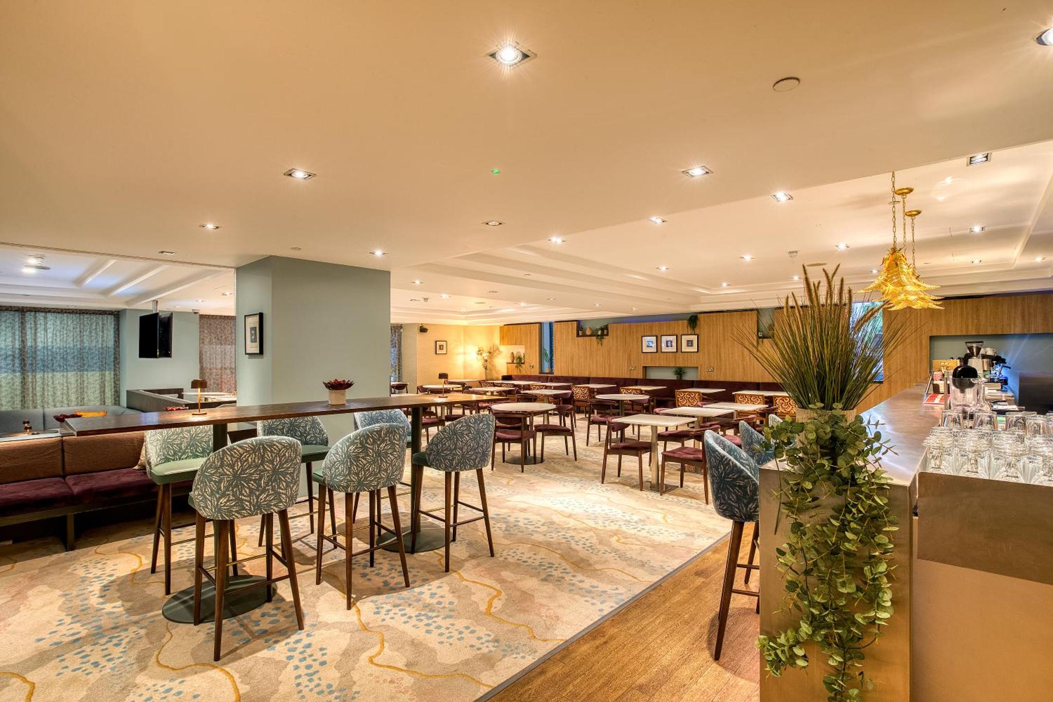 a restaurant with tables and chairs and a bar at Hilton London Kensington Hotel in London