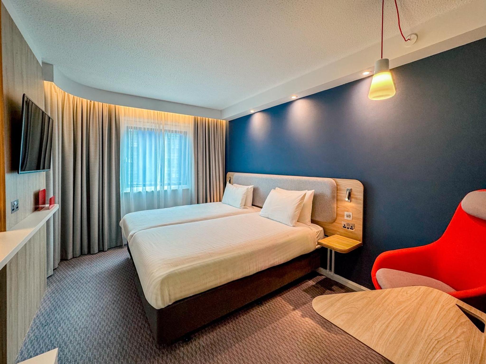 a hotel room with a bed and a red chair at Holiday Inn Express London Stratford by IHG in London +74 photos