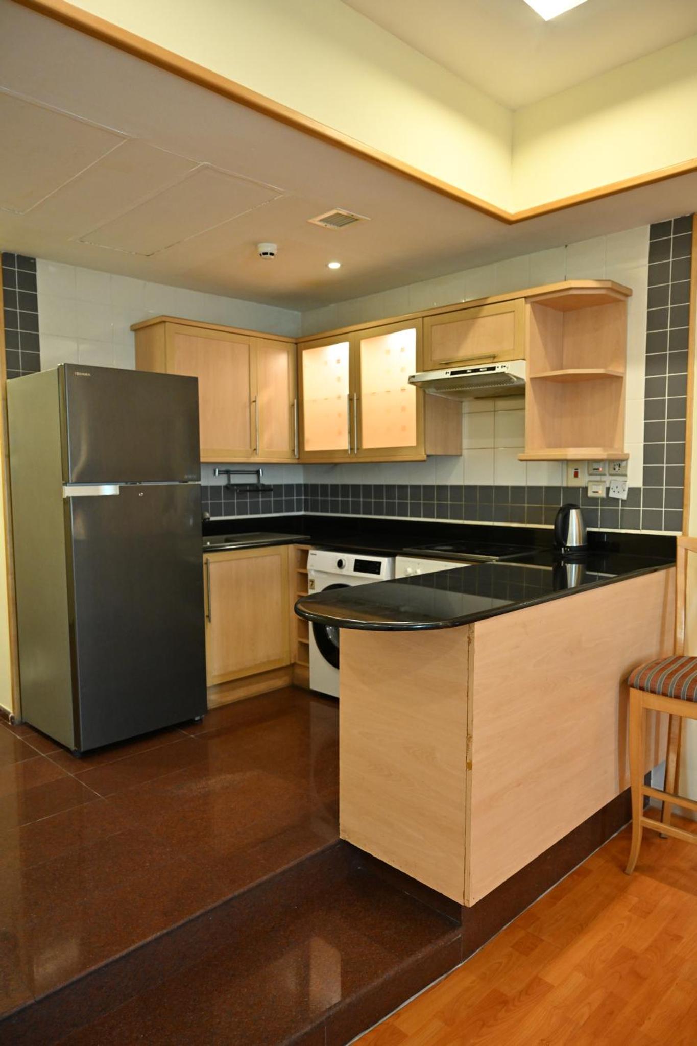 a kitchen with a stainless steel refrigerator and wooden cabinets at One Pavilion Luxury Serviced Apartments in Manama