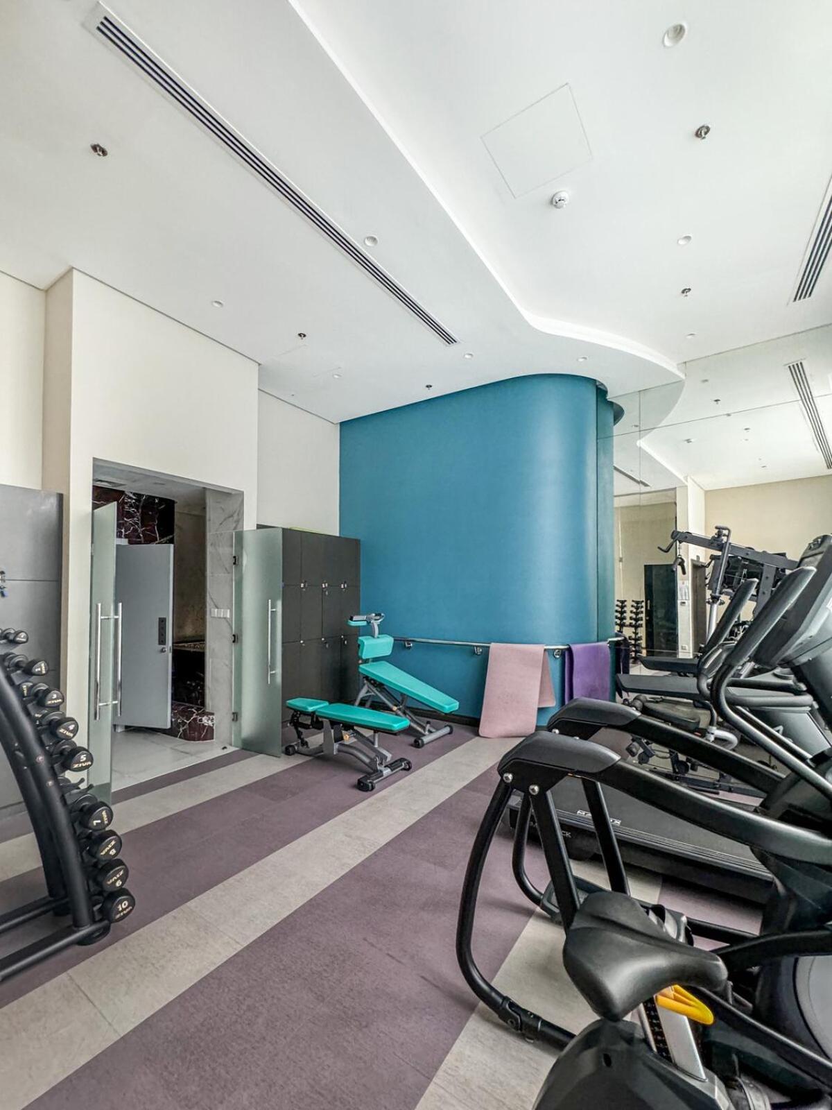 a gym with treadmills and a blue wall at 2BR Four Season View in Water Bay in Manama