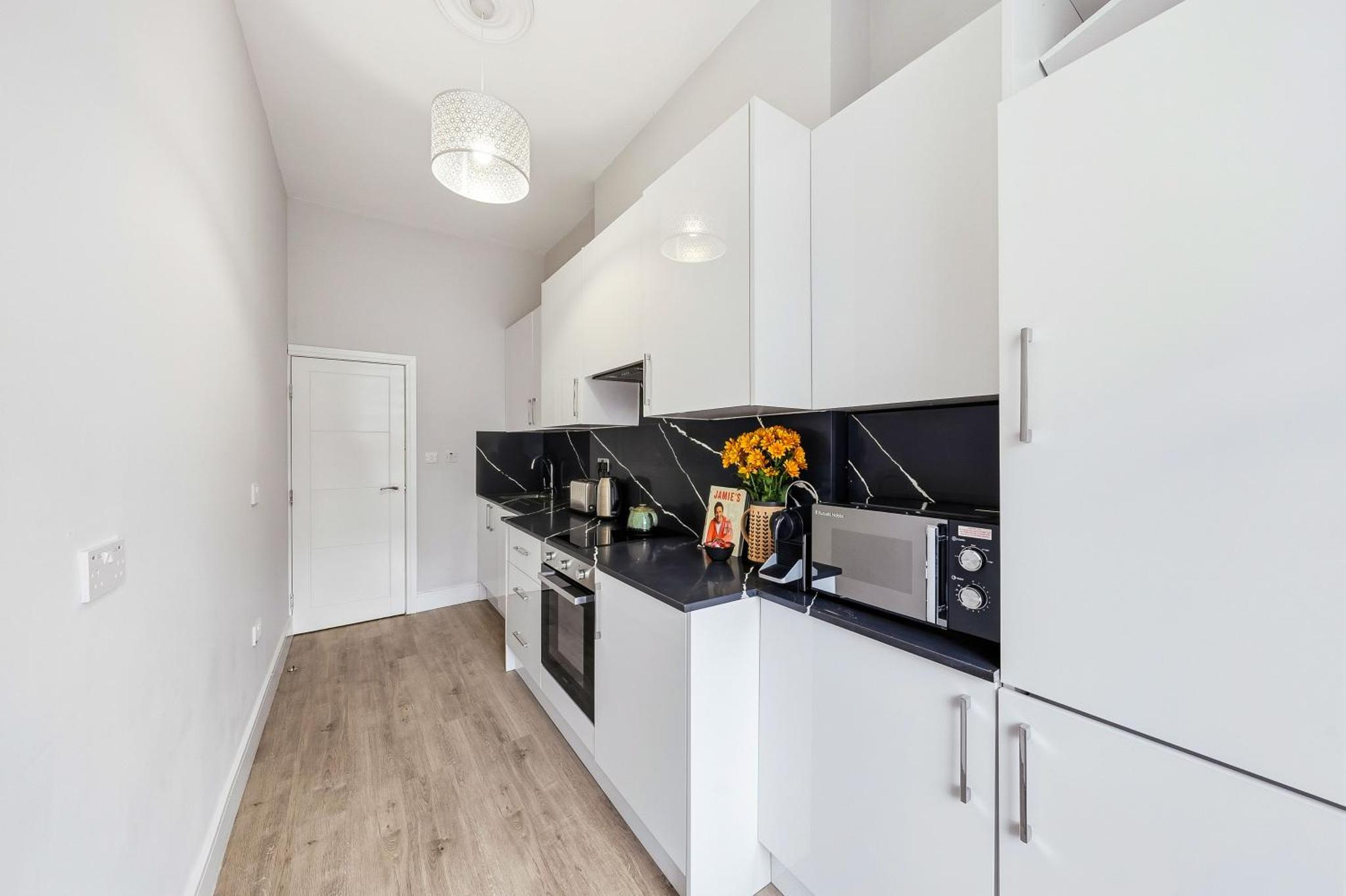 a kitchen with white cabinets and black counter tops at Bright & Stylish Flat in the Heart of Islington in London