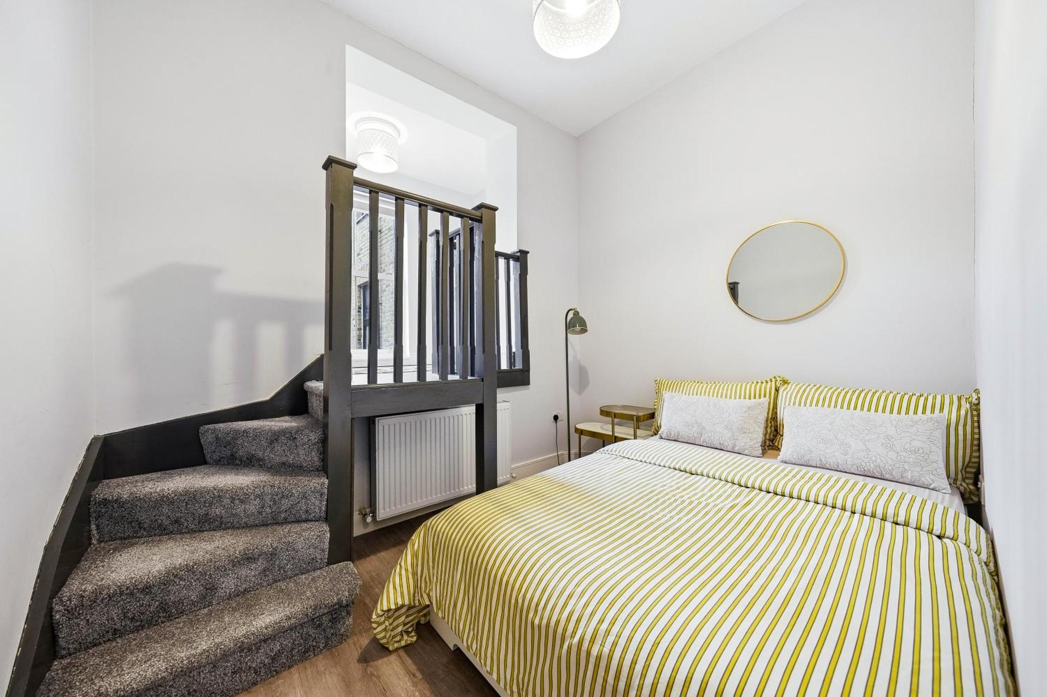 a bedroom with a bed and a staircase with a mirror at Bright & Stylish Flat in the Heart of Islington in London