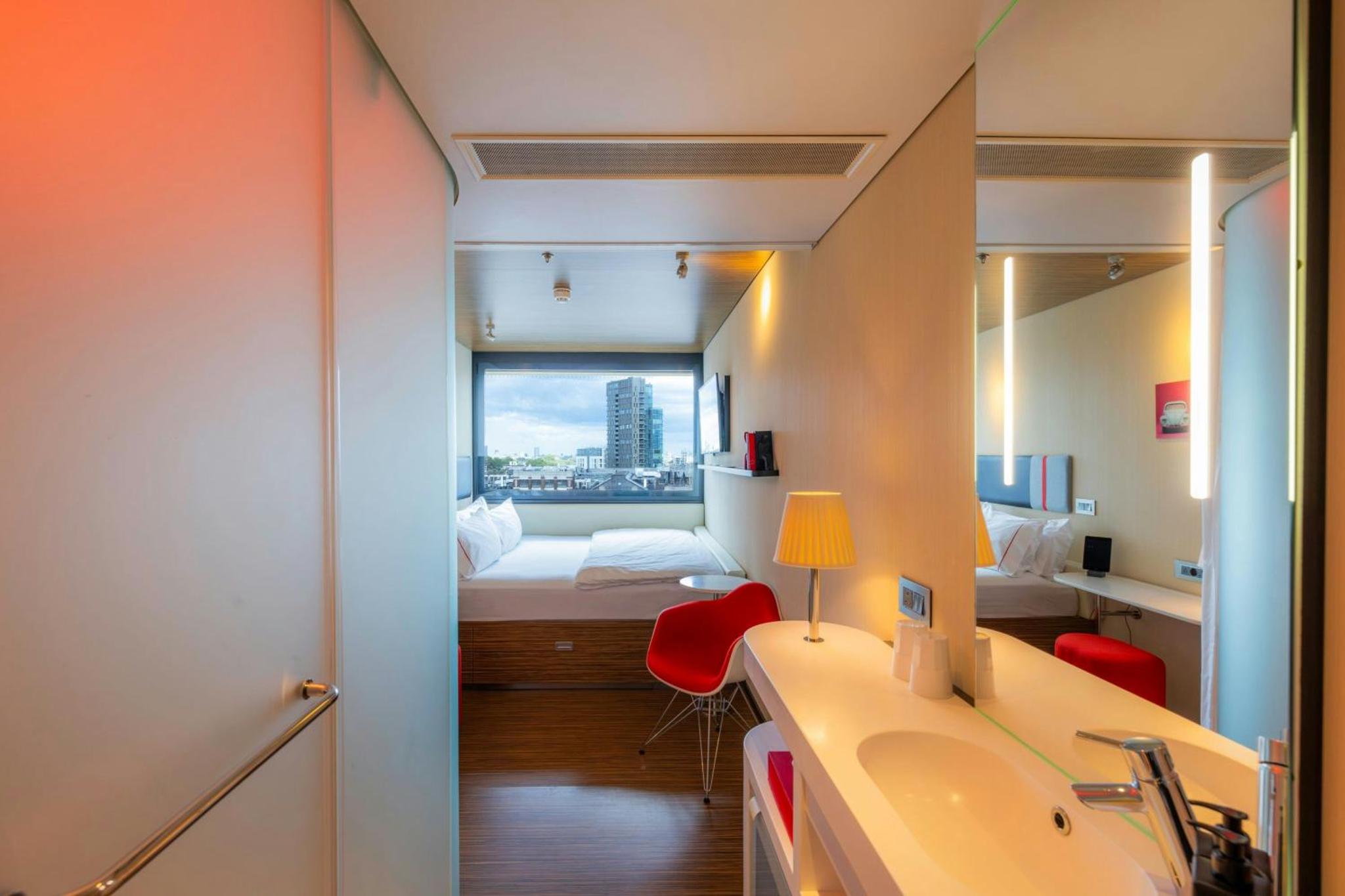 a bathroom with a sink and a bed with a window at citizenM London Shoreditch in London