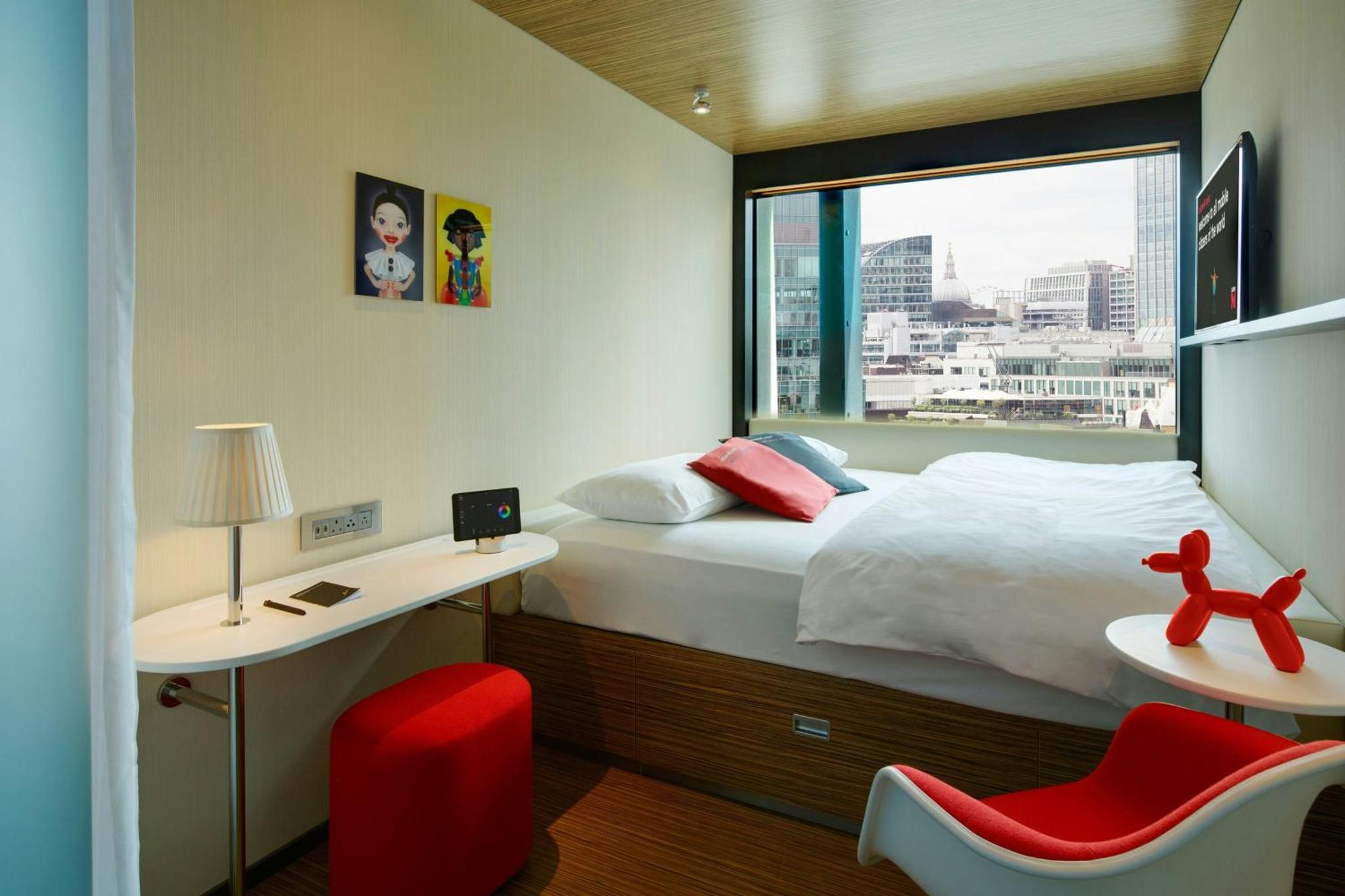 a bedroom with a bed with a window and a red chair at citizenM London Shoreditch in London