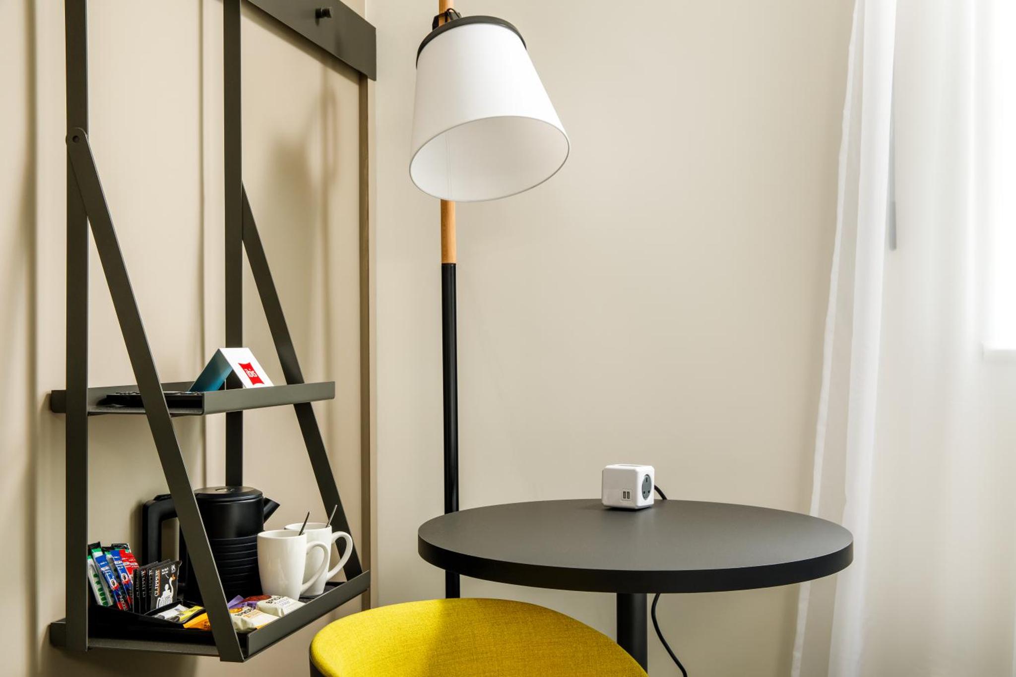 a table and a lamp next to a yellow chair at ibis London Greenwich in London
