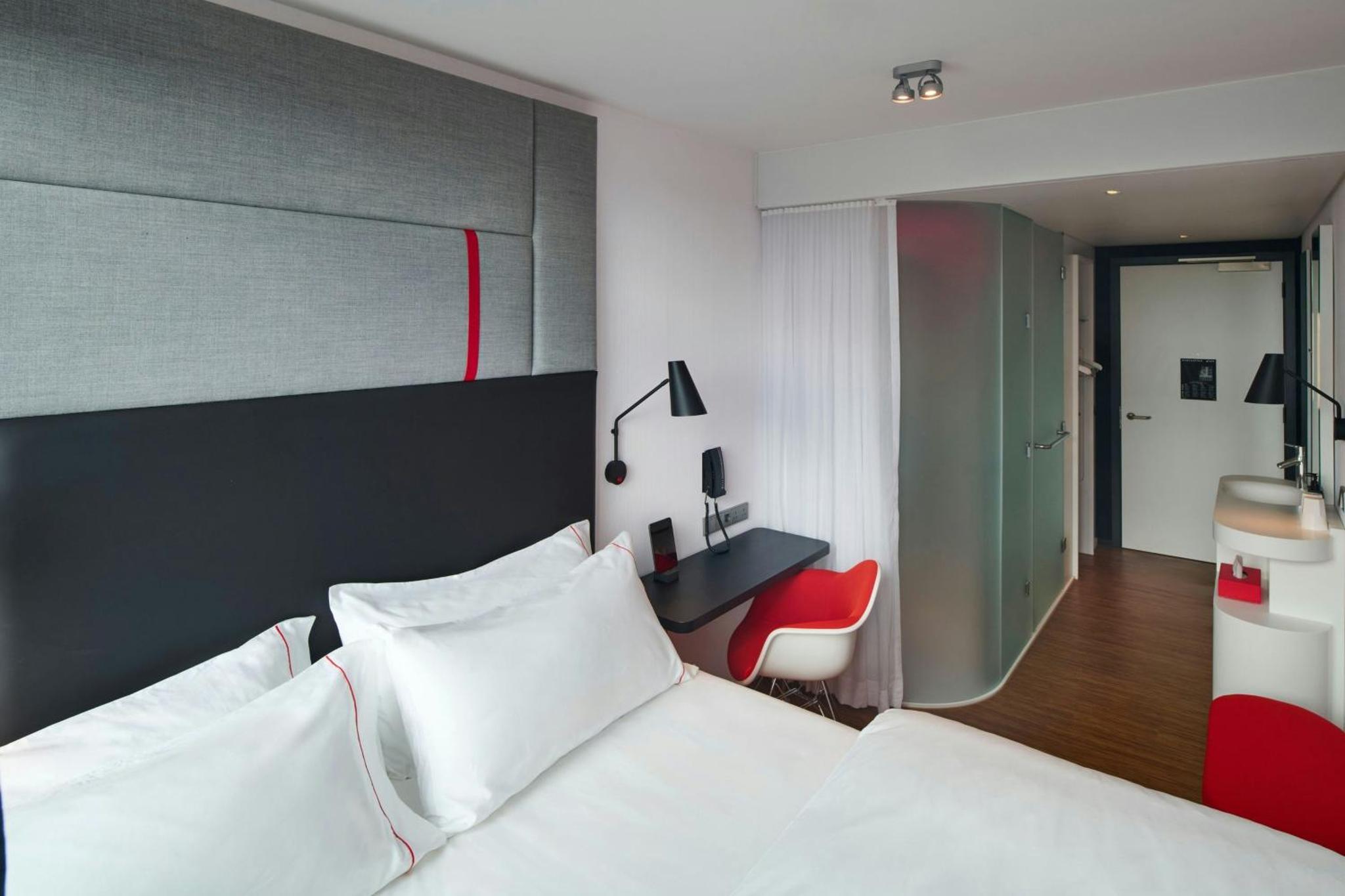 a bedroom with a white bed and a red chair at citizenM London Victoria Station in London