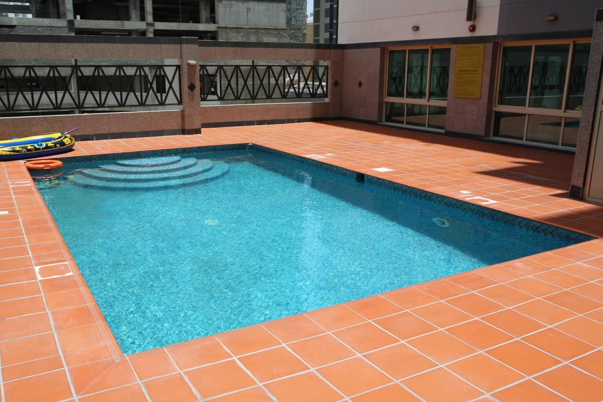 a swimming pool with a tiled floor and a building at Desert Pearl Hotel Apartment in Manama