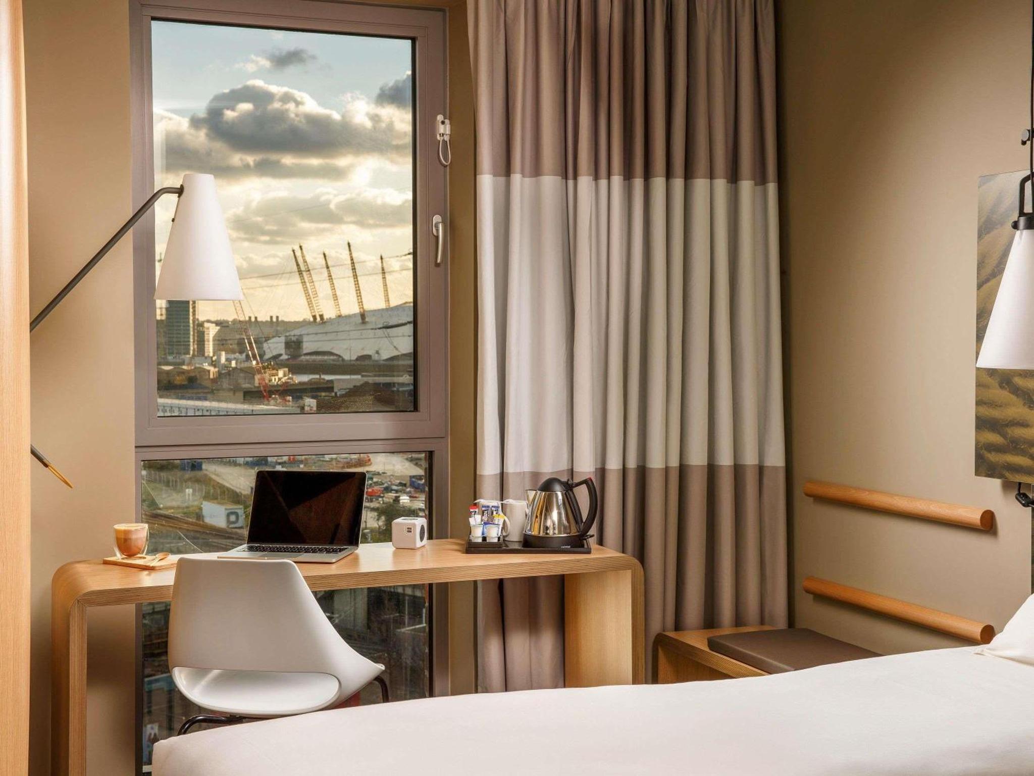 a hotel room with a desk with a laptop and a window at ibis London Canning Town in London