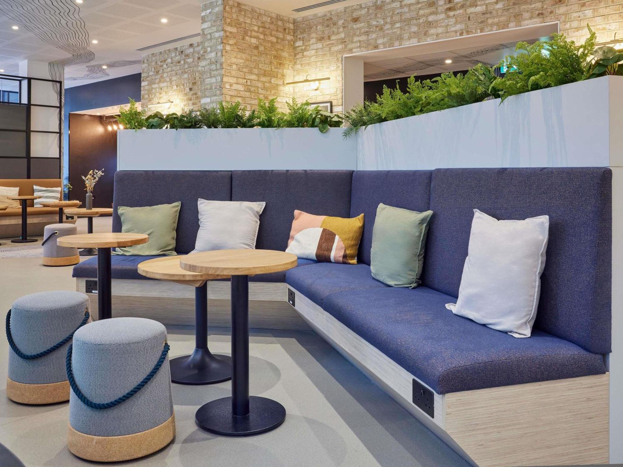 a blue couch with pillows and tables and plants at Aparthotel Adagio London City East in London