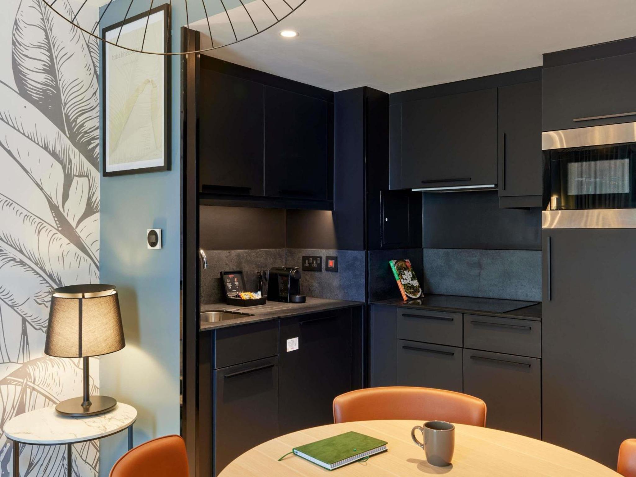 a kitchen with black cabinets and a table with orange chairs at Aparthotel Adagio London City East in London