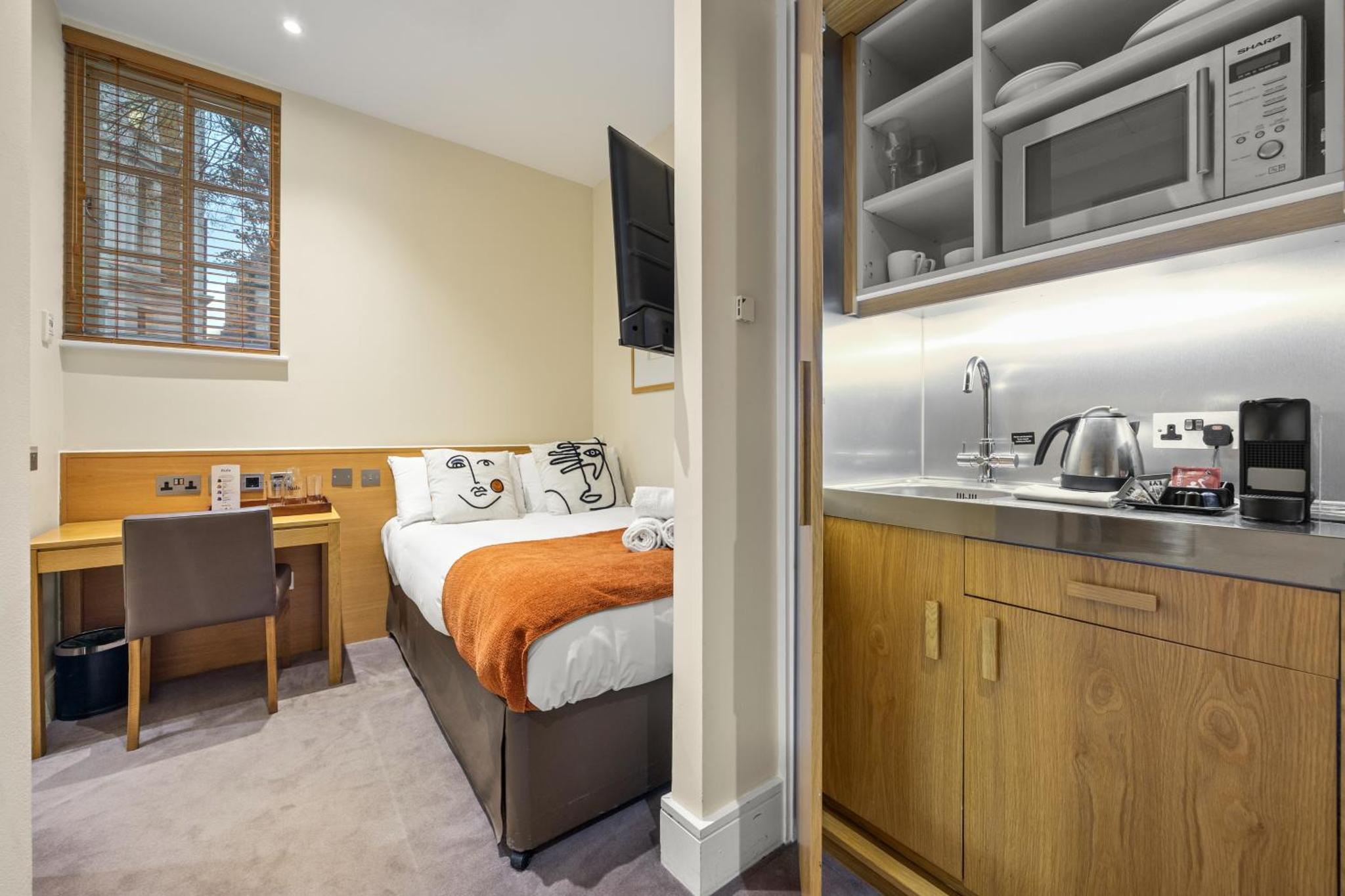a bedroom with a bed and a kitchen with a sink at Stay Kula London - Kensington in London