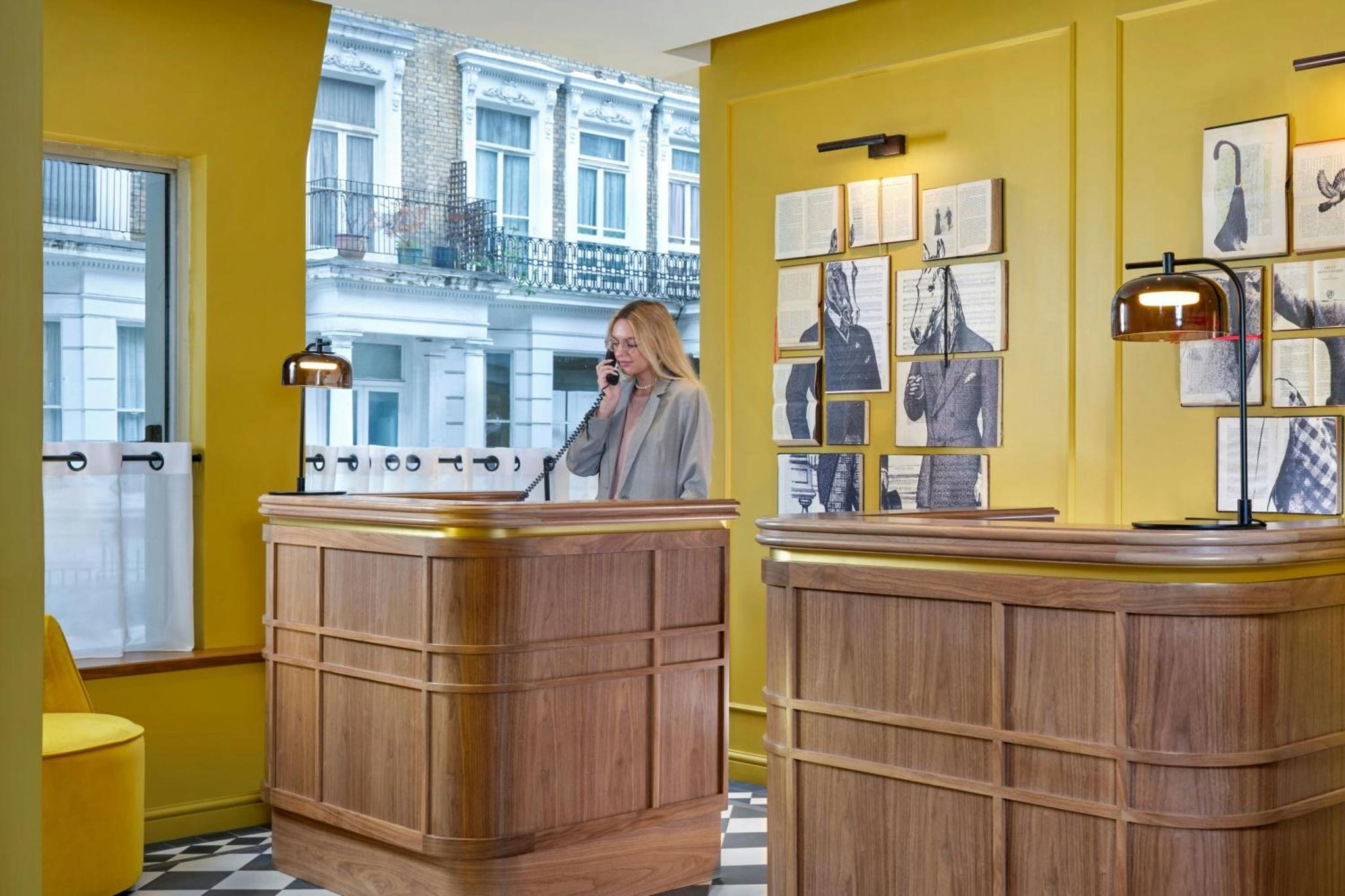 a woman talking on a cell phone behind a counter at The Cura Hotel Kensington, London, a Tribute Portfolio Hotel in London