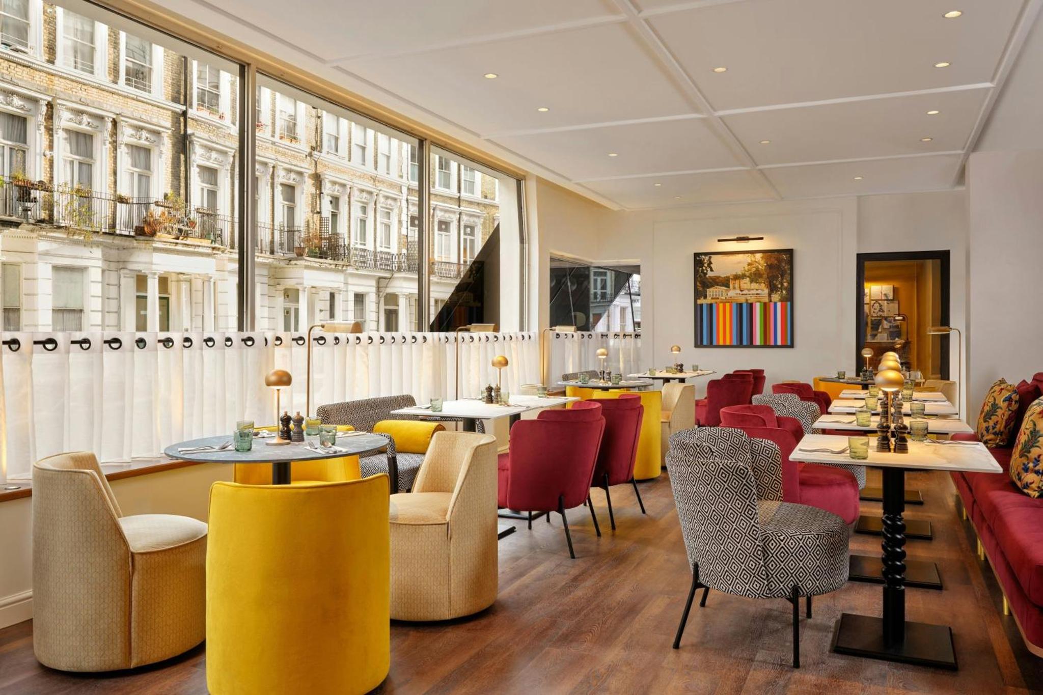 a restaurant with tables and chairs and windows at The Cura Hotel Kensington, London, a Tribute Portfolio Hotel in London