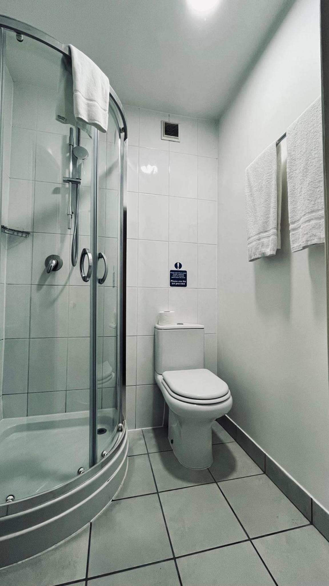 a bathroom with a toilet and a glass shower at Arriva Hotel in London +36 photos