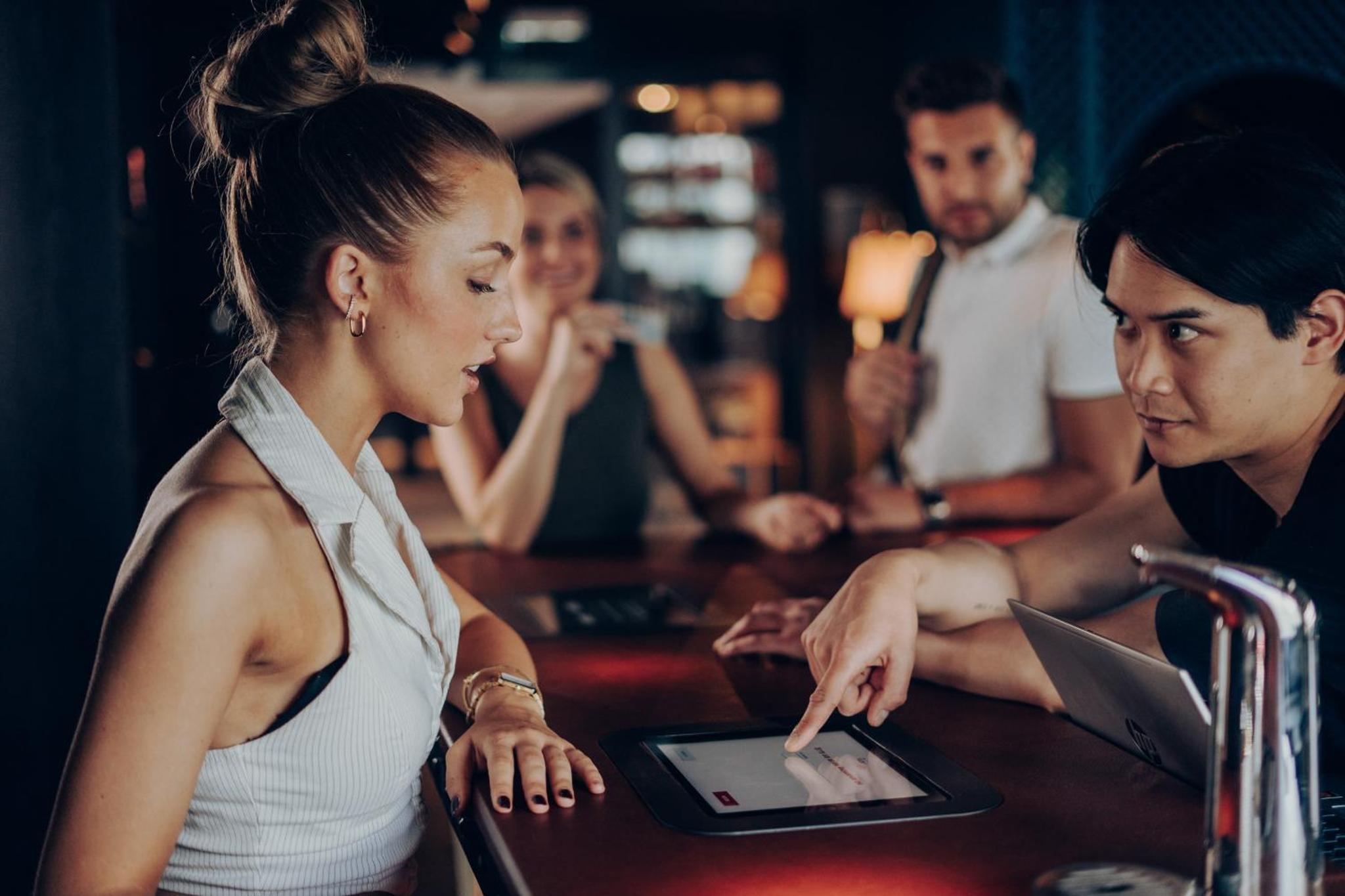 a woman sitting at a table with a man using a tablet at Ruby Lucy Hotel London by IHG in London