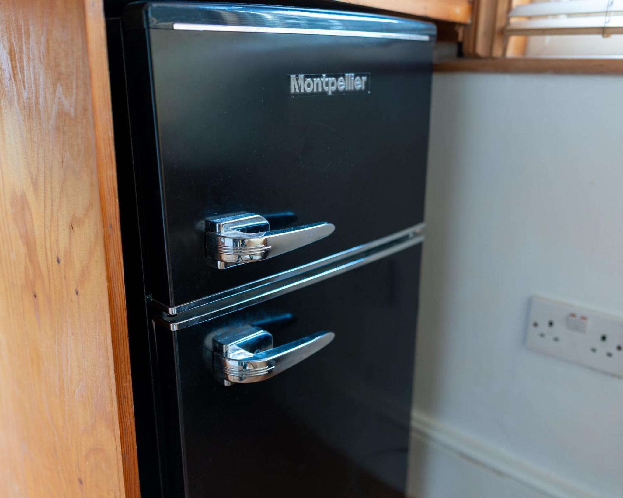 a black refrigerator with two silver handles in a kitchen at Studio apartment next to Highgate tube station in London +2 photos