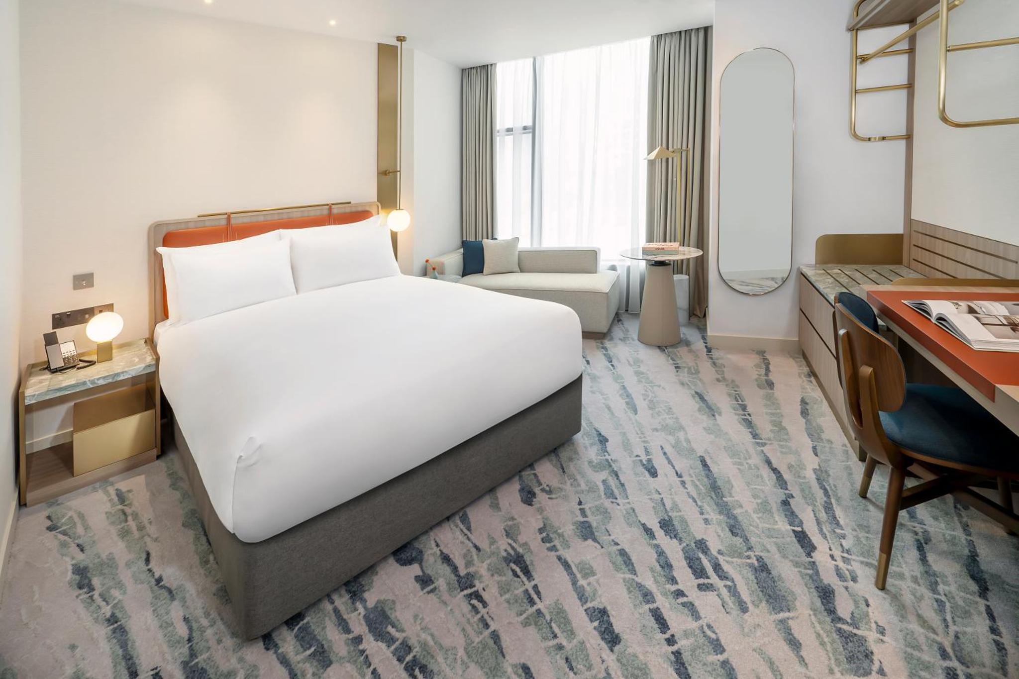 a hotel room with a large white bed and a desk at Dorsett Hotel Canary Wharf in London